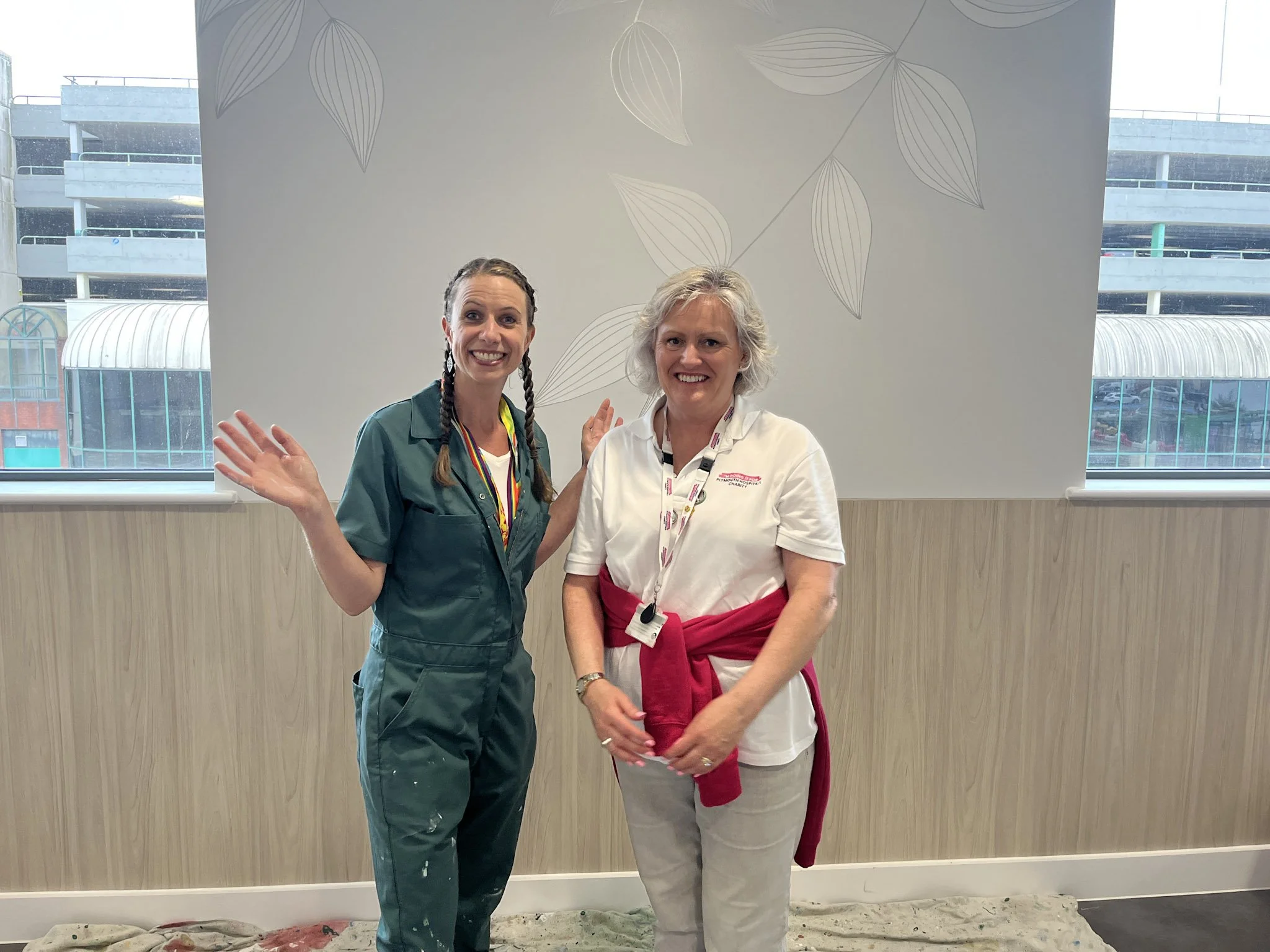 Picture of Ellie (Mrs Murals) smiling with Bernie, the Charity Engagement Coordinator, in front of the painted wall at the CDC.