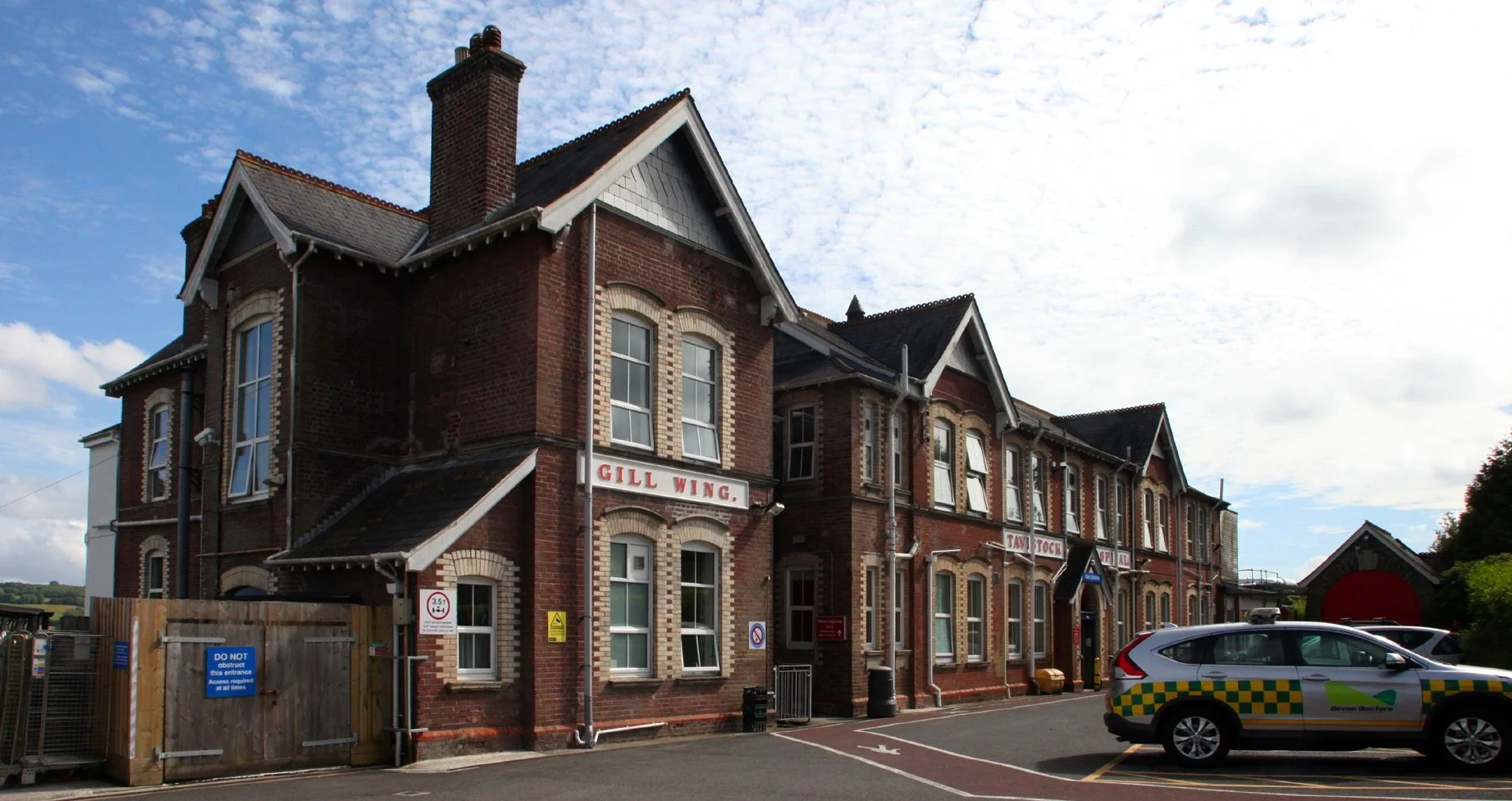 A historic brick building labeled Gill Wing, with a police vehicle parked in front, under a partly cloudy sky.