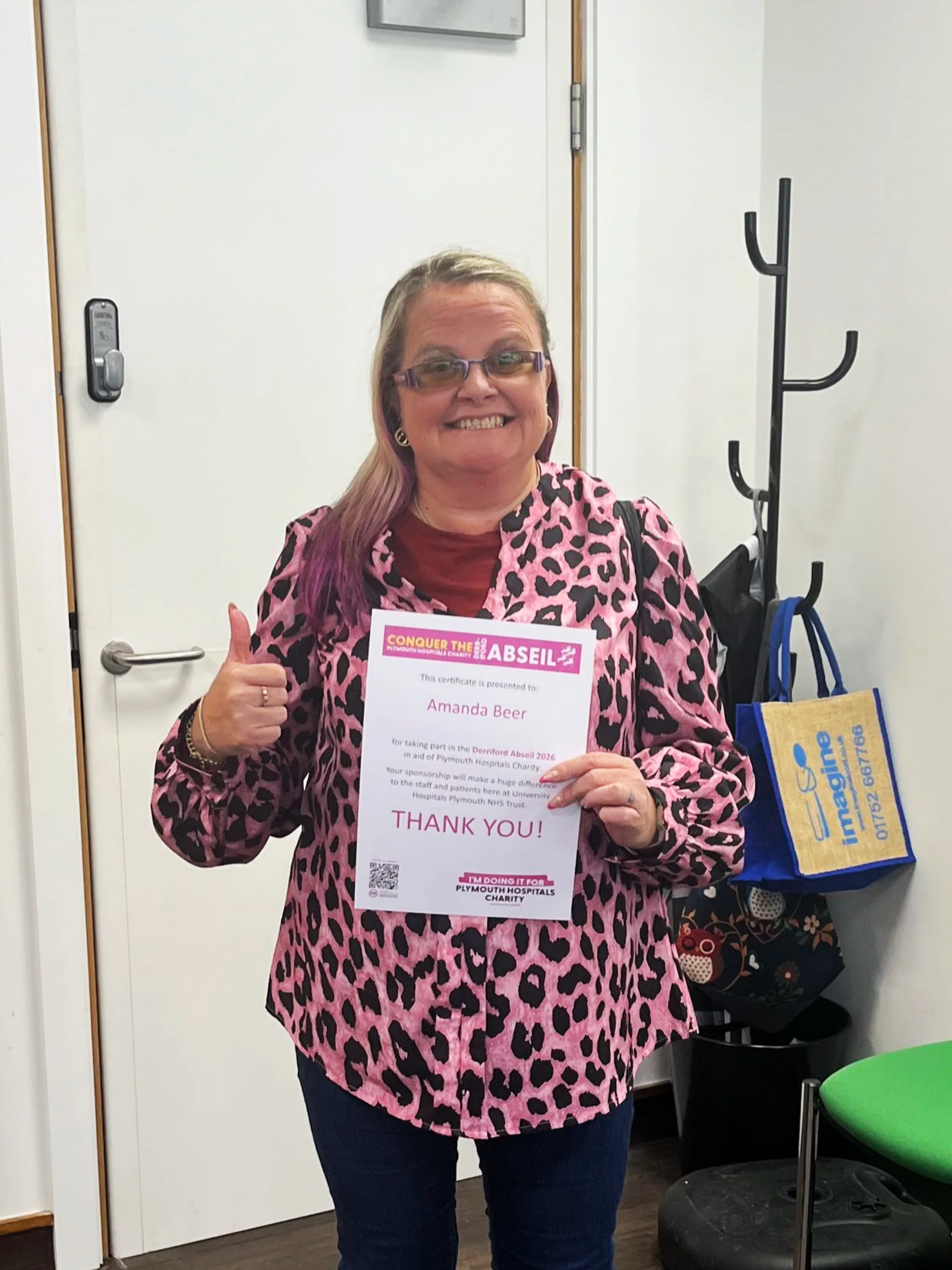A photo of Amanda. She's smiling with one thumb up and holding her certificate after completing the abseil.
