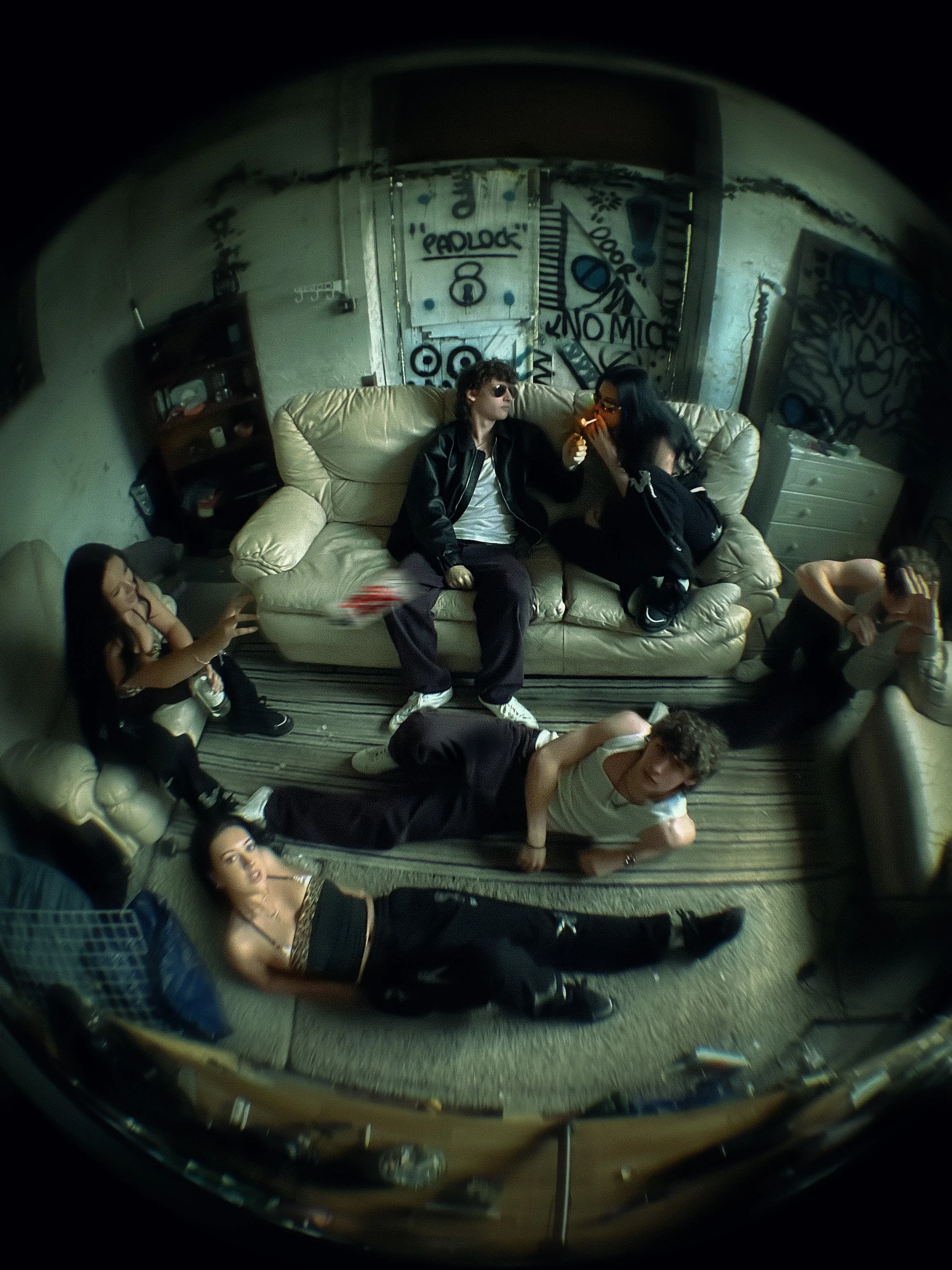 Group of young adults hanging out in a grungy, graffiti-covered room with a lens distortion effect.