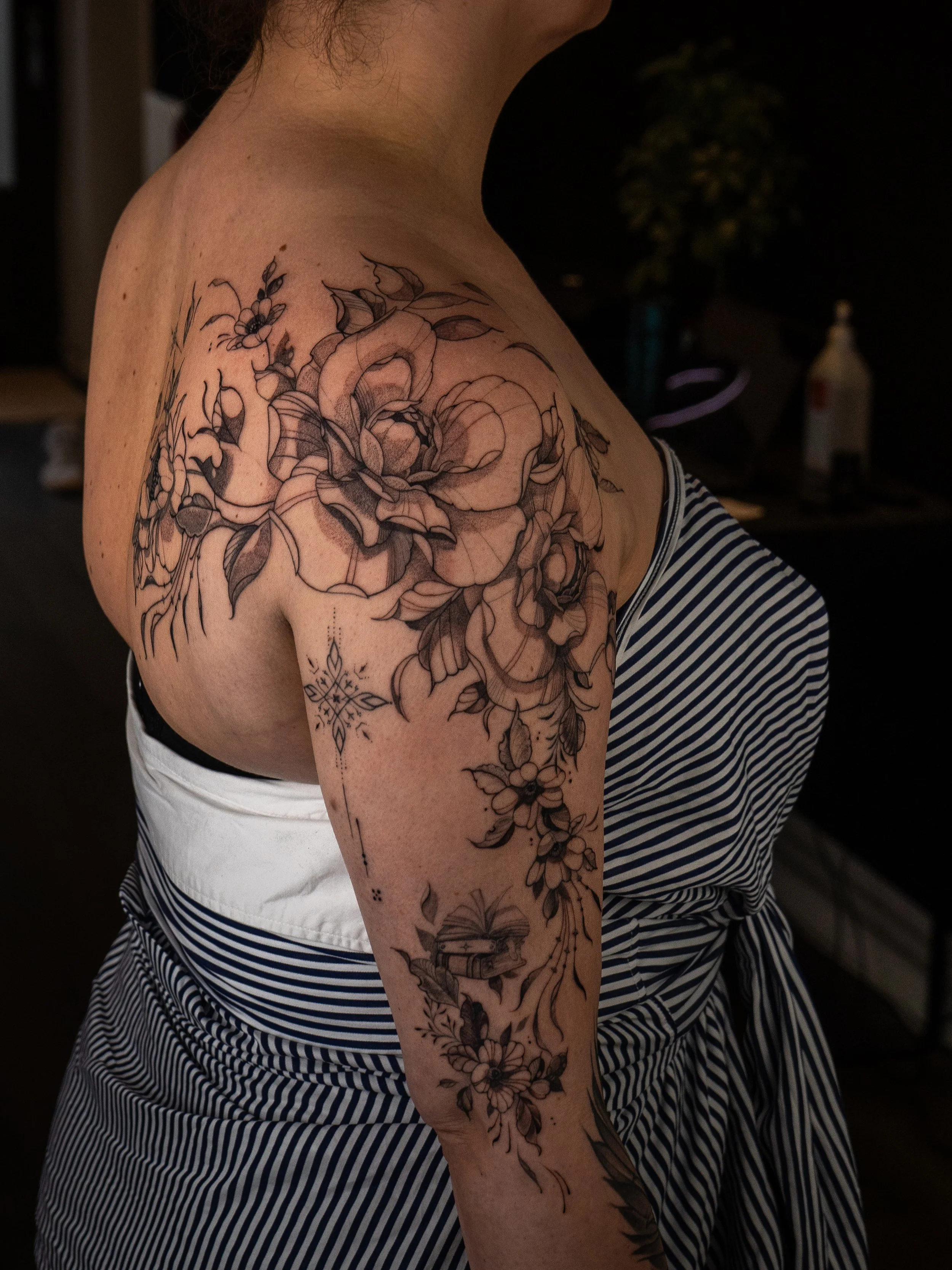 En person med en stor blommig tatuering på axeln och armen, klädd i en svart och vit randig klänning.