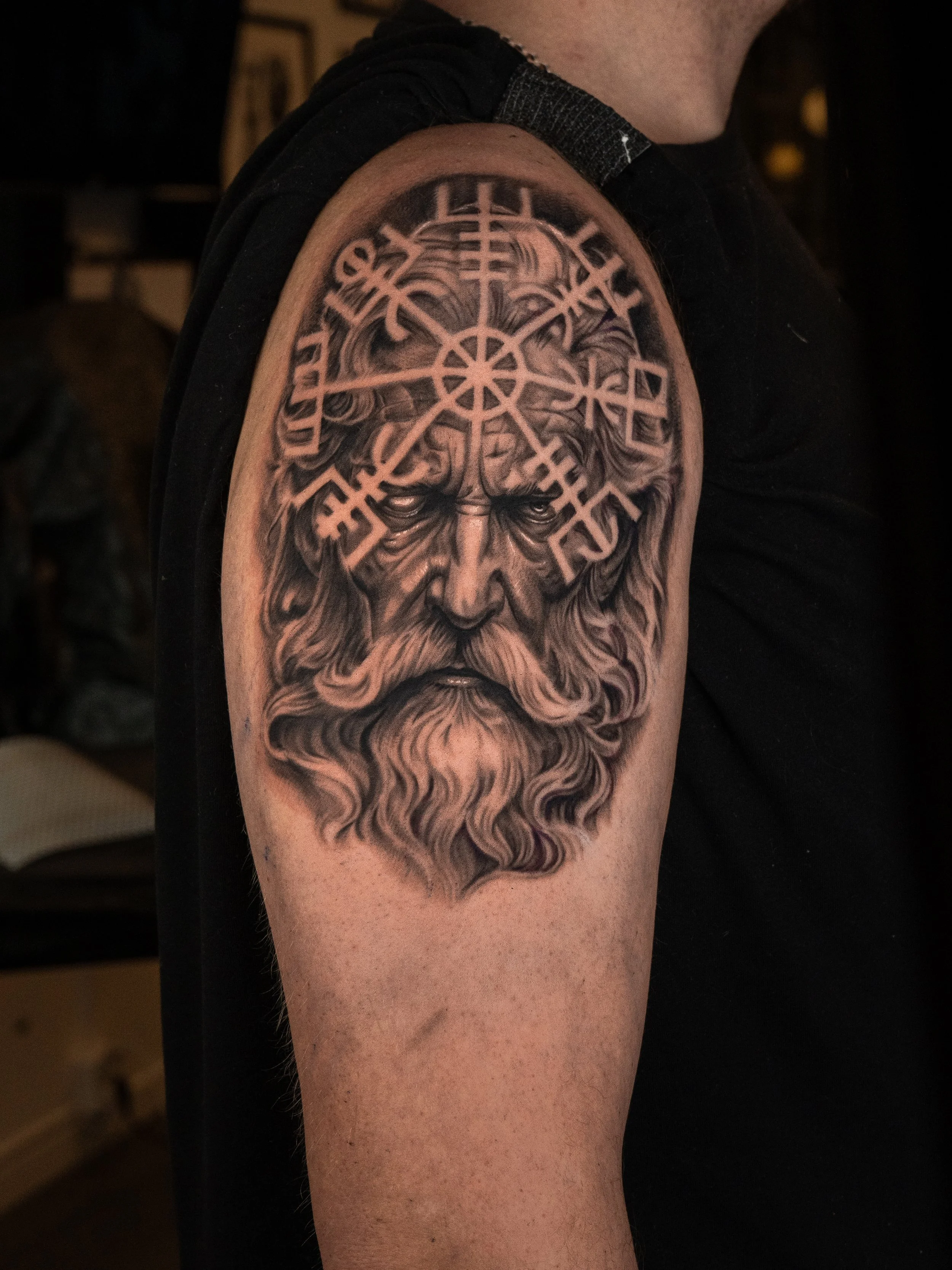 Tatuerad bild av en bearded man med ett fönster av runor eller symboler ovanför huvudet.
