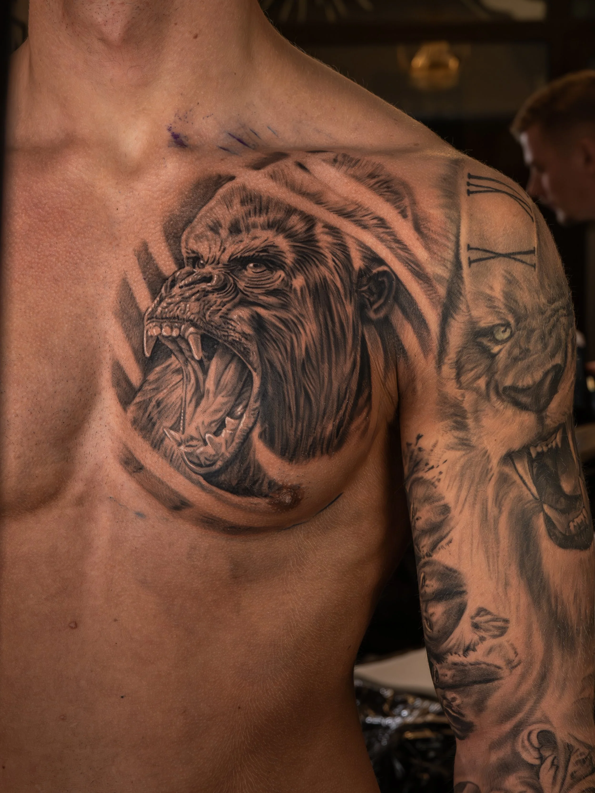 Tatuering av en ilska lejon på vänster axel och även delar av ett ansikte av ett annat lejon på armen.