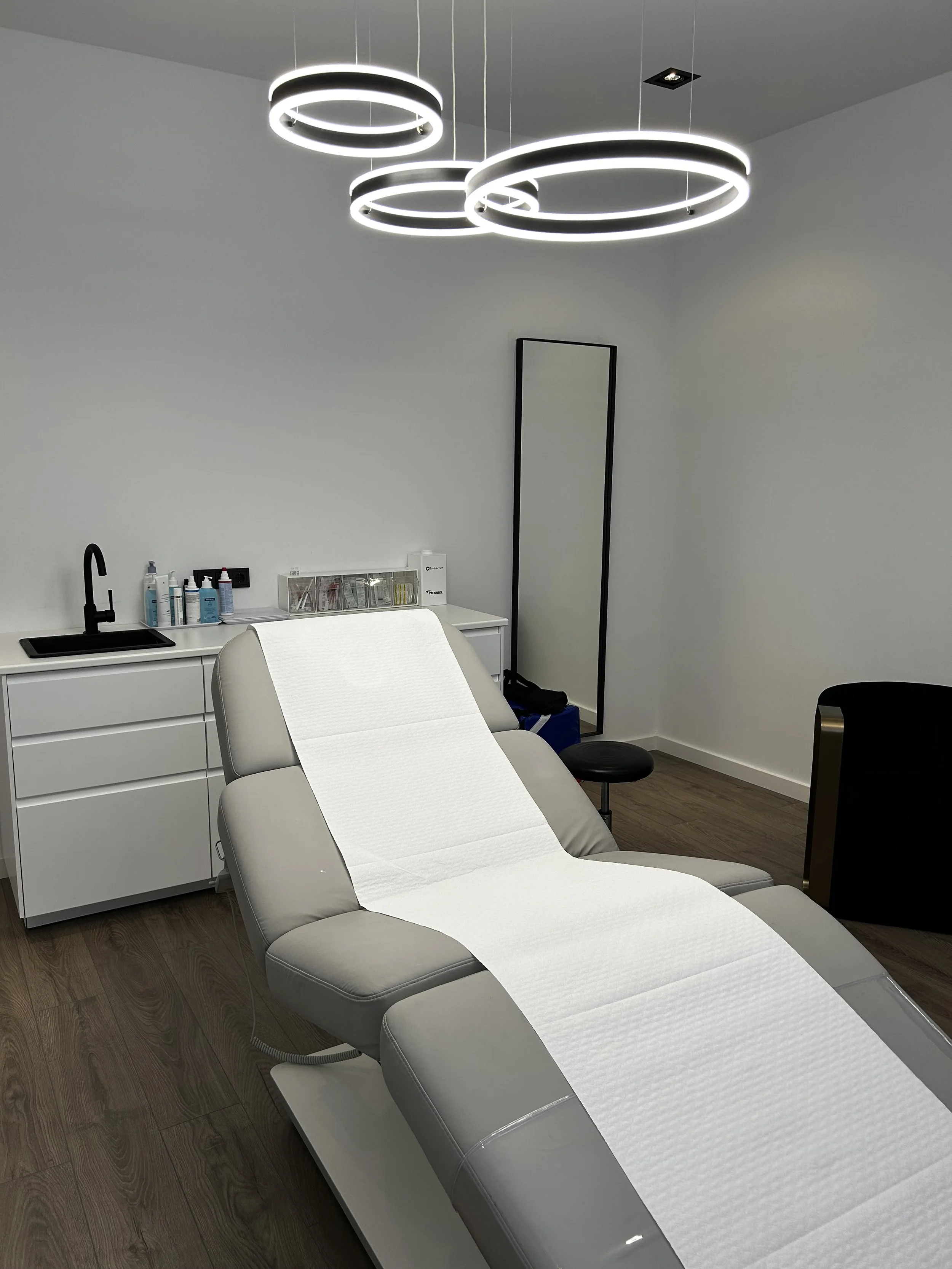 Ein Behandlungsstuhl in einem Behandlungsraum, einer Arztpraxis für ästhetische Chirurgie umgeben von medizinischen Geräten und Beleuchtung.