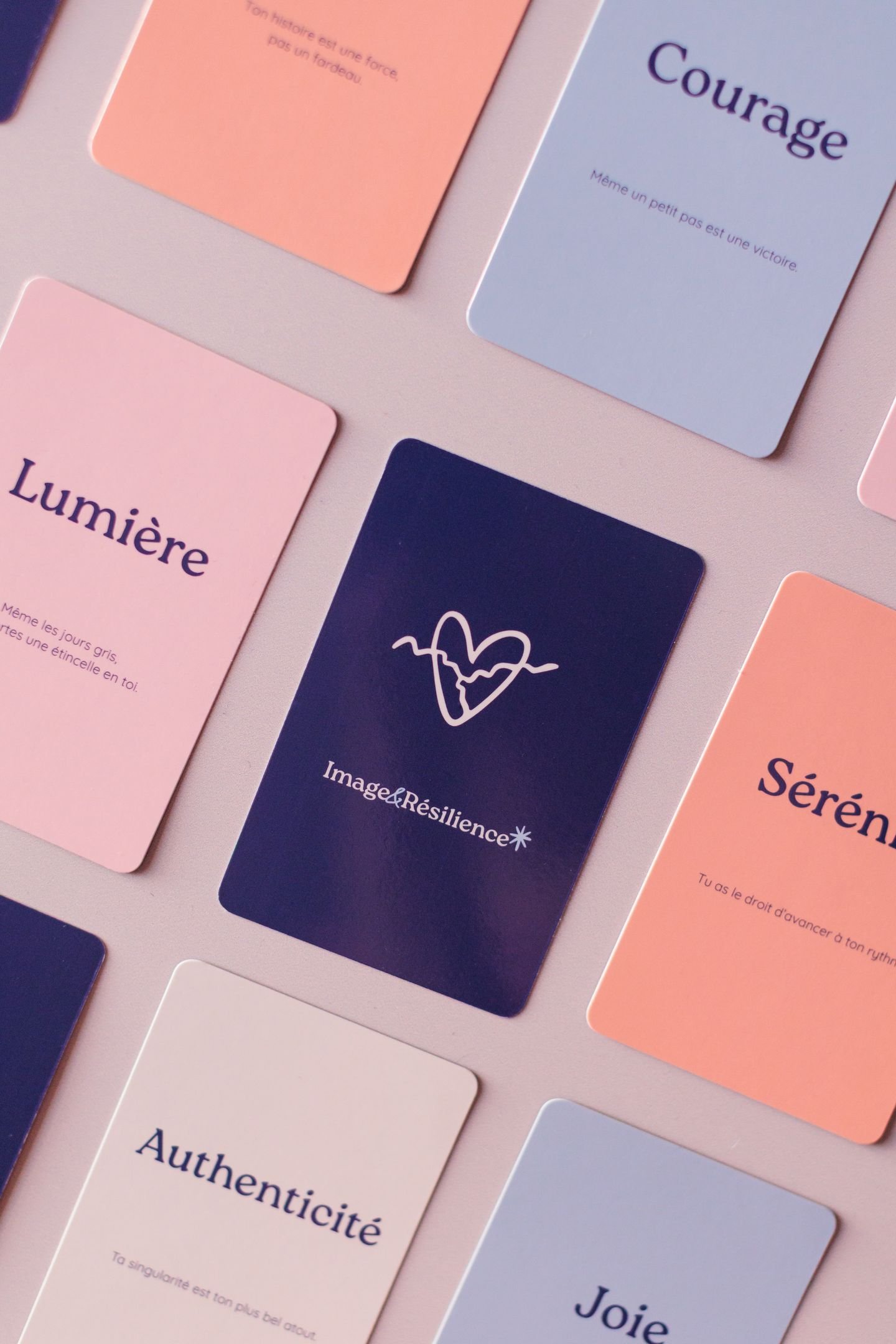 Recto de plusieurs cartes de tarot ou de développement personnel avec des mots en français comme Courage, Lumière, Sérénité, Authenticit e9, Joie, Image&R e9silience, dispos e9es sur un fond rose clair.
