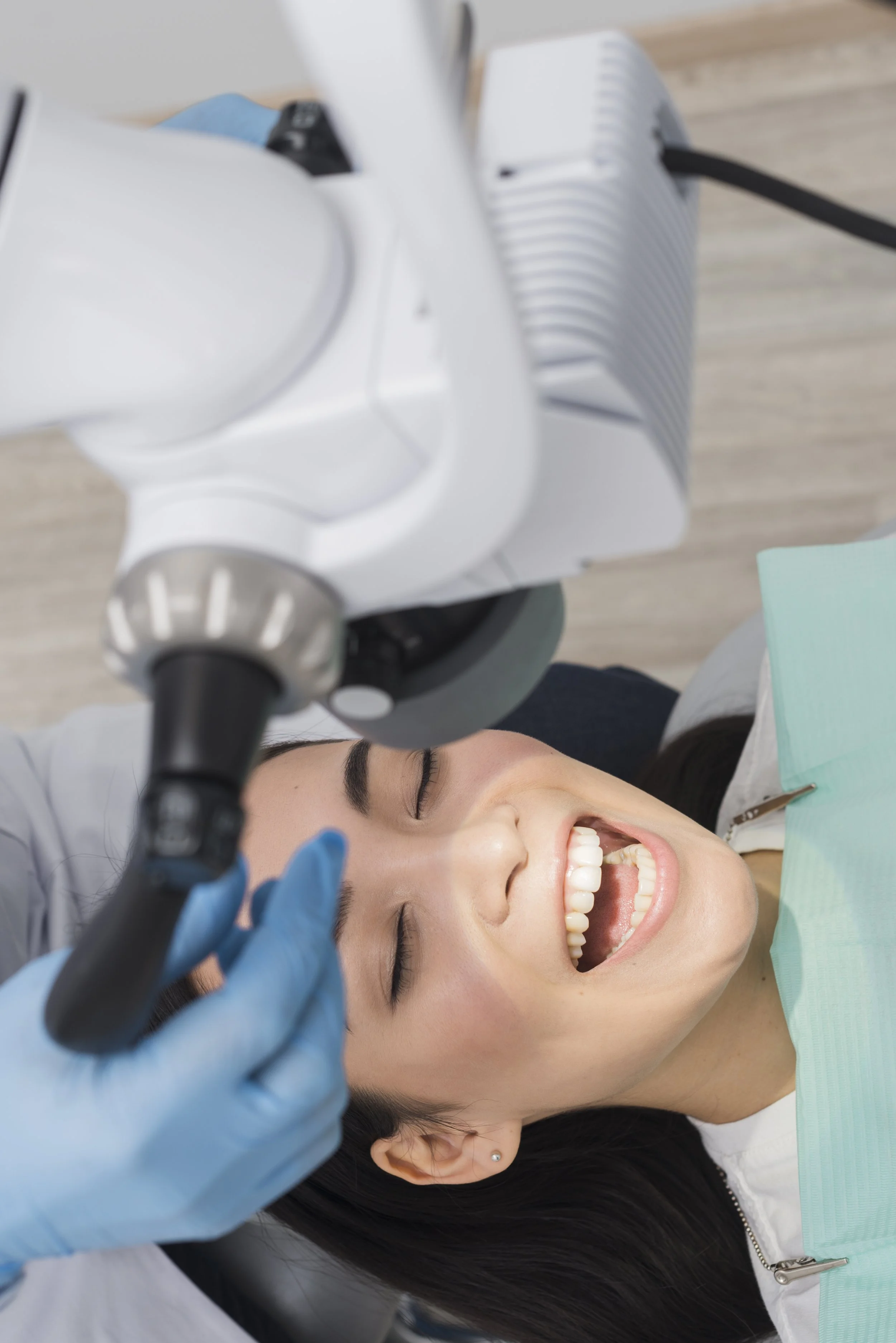 A woman smiling with her mouth open during a dental examination, with a dentist's hand holding a dental tool above her.