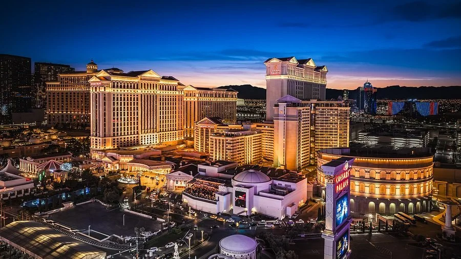 Night view of the Las Vegas Strip with illuminated hotels and casinos, including the Venetian and Resorts World, against a dark blue sky.