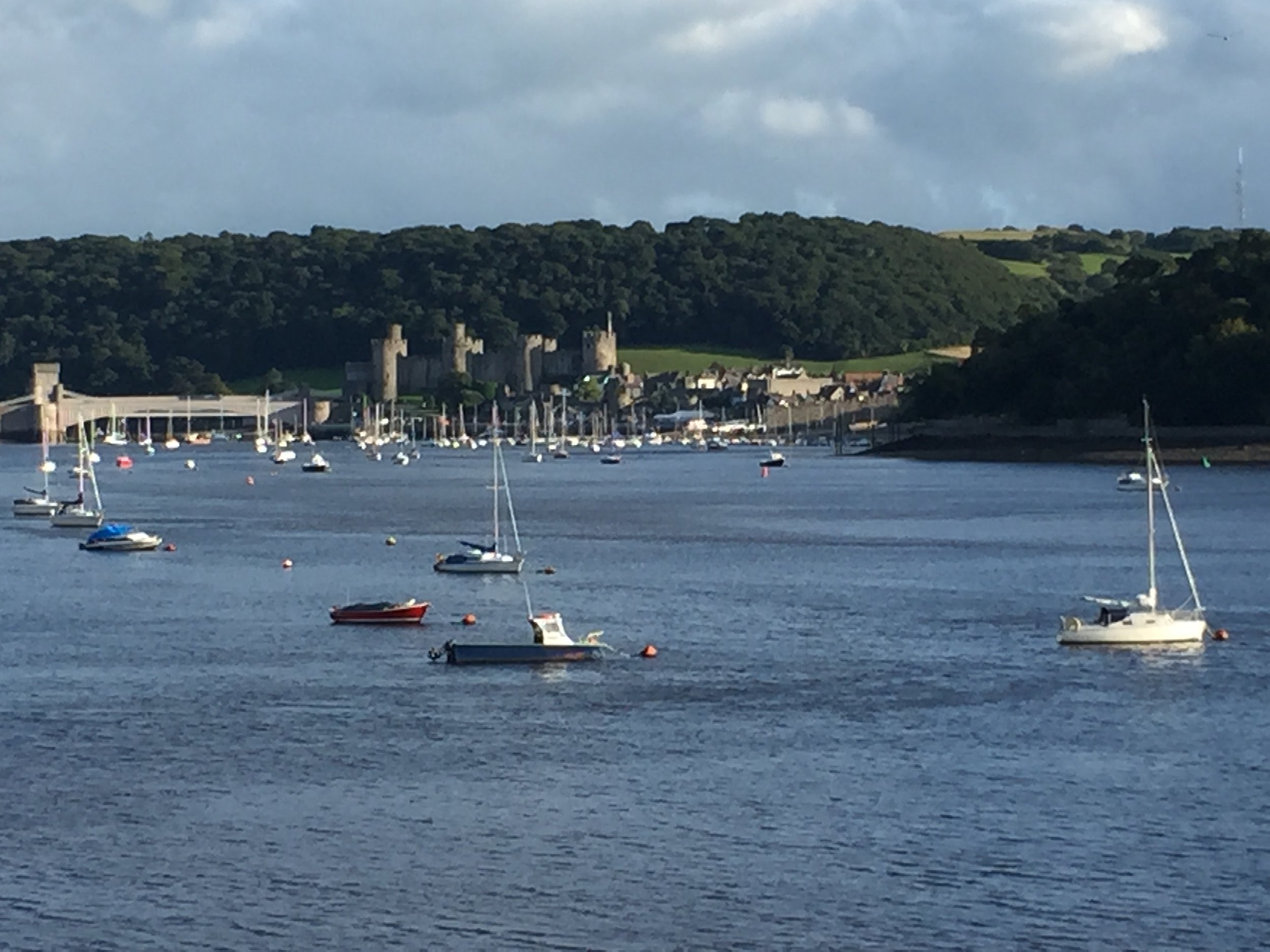 A harbor with boats floating on the water, a castle on a hill, and cloudy skies.