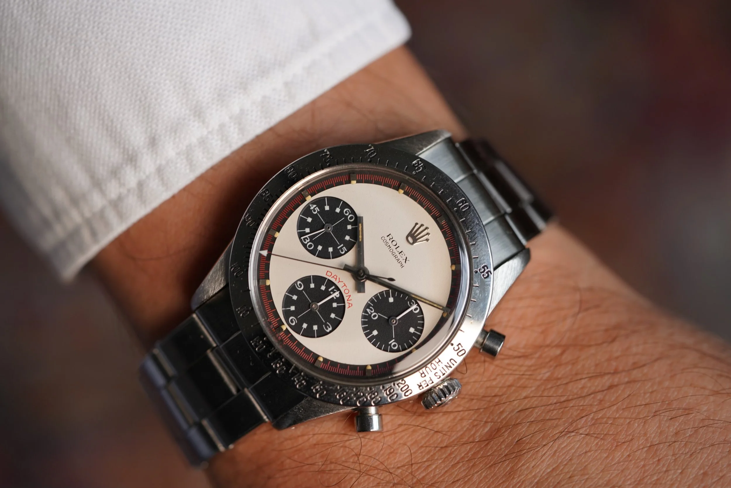 A Rolex Cosmograph Daytona wristwatch with a black bezel and white dial, featuring three black subdials and a red "Daytona" label, worn on a person's wrist.