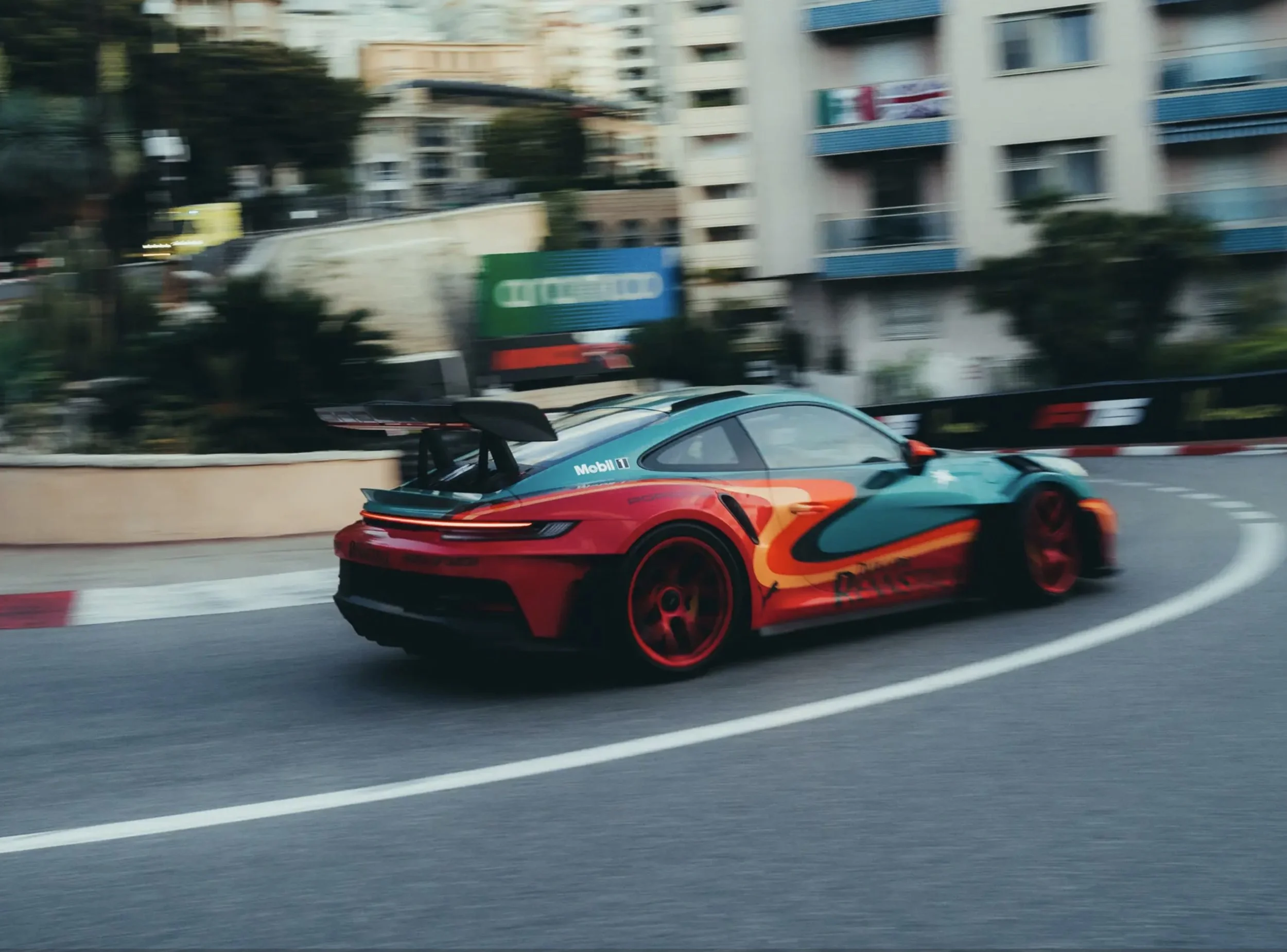 A colorful Porsche racing car with a rear spoiler driving on a city street curve.