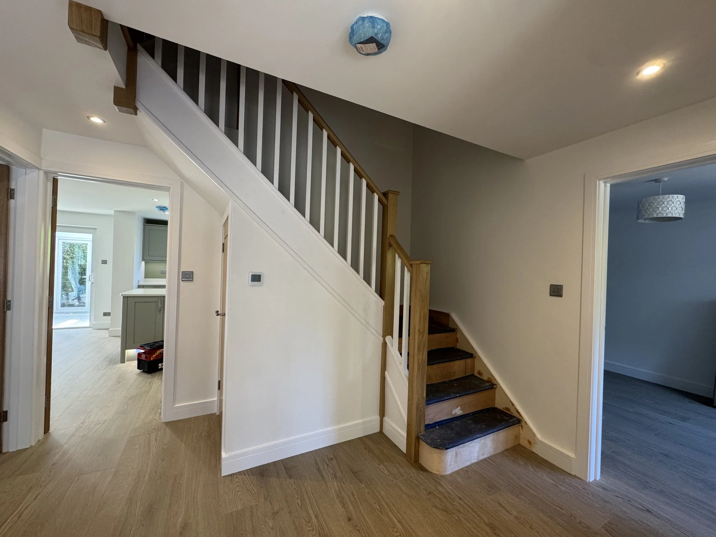 Interior of a house with a staircase under construction, wooden steps, white walls, and doorways leading to other rooms.
