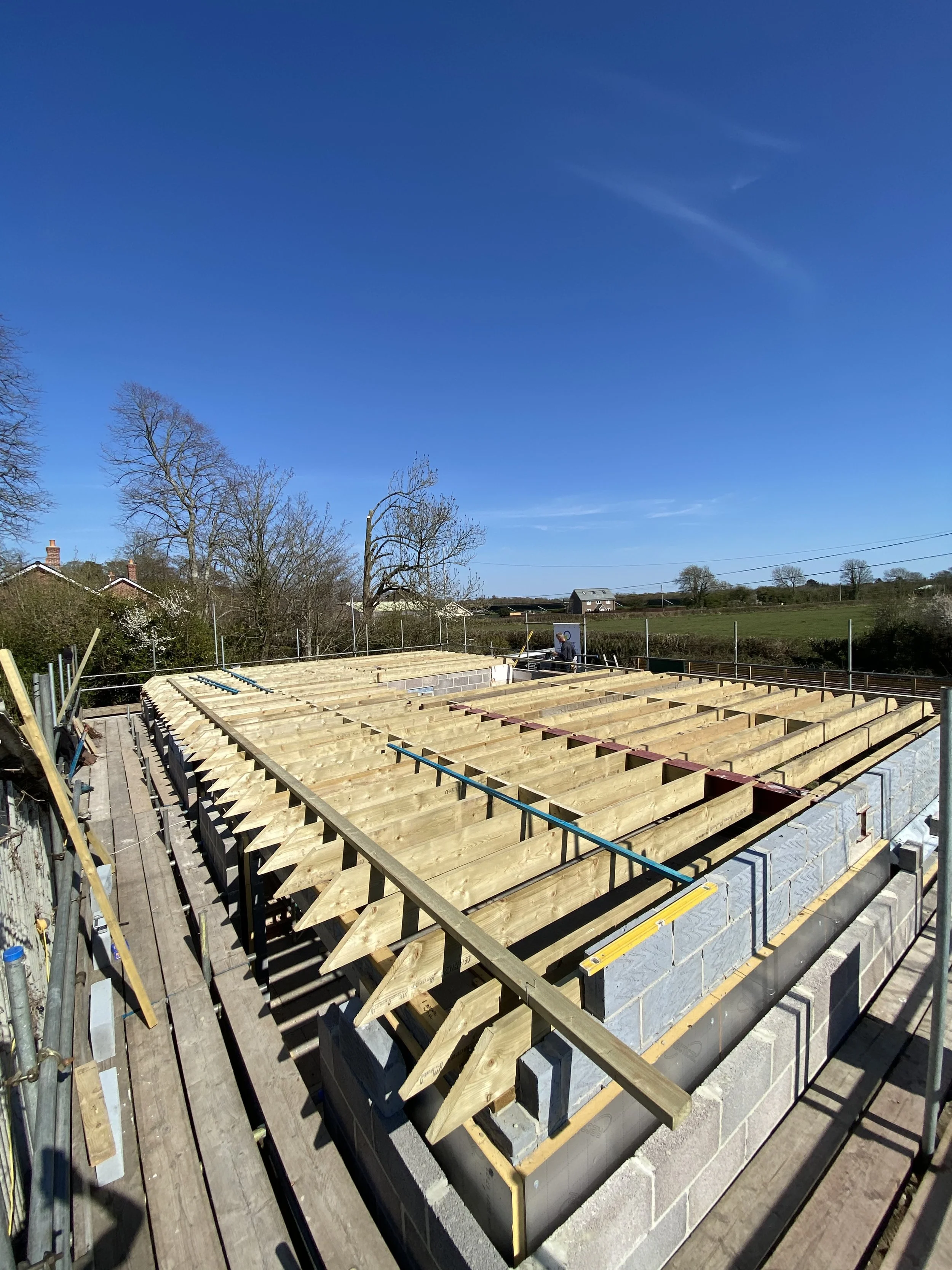 Construction site with wooden beams and concrete blocks, part of building framing under blue sky.