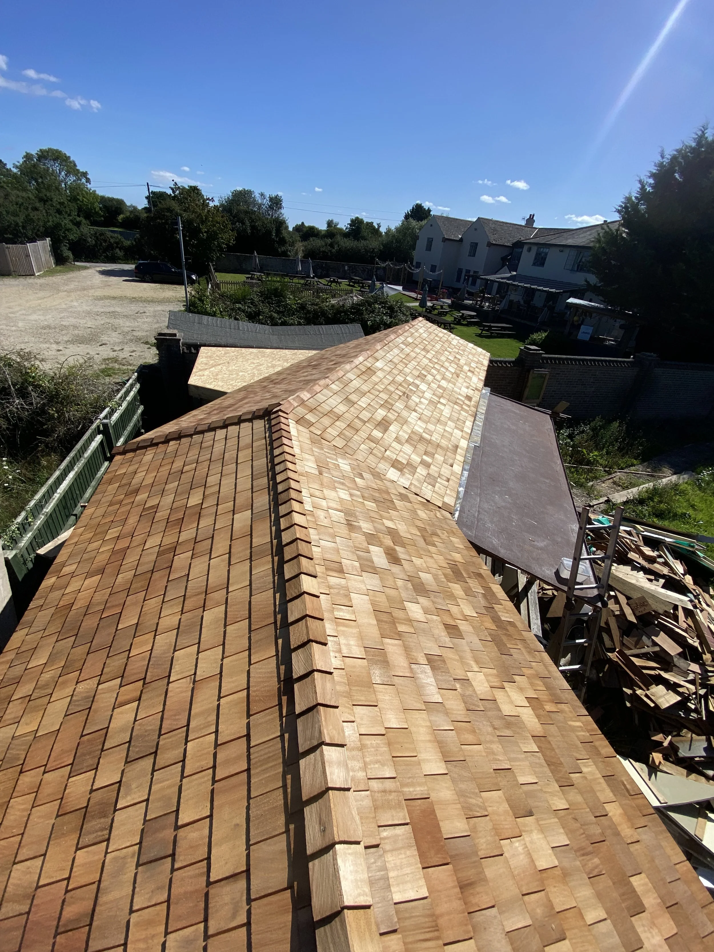 View of a newly installed wooden shingle roof on a building, with an outdoor area and neighboring houses in the background.
