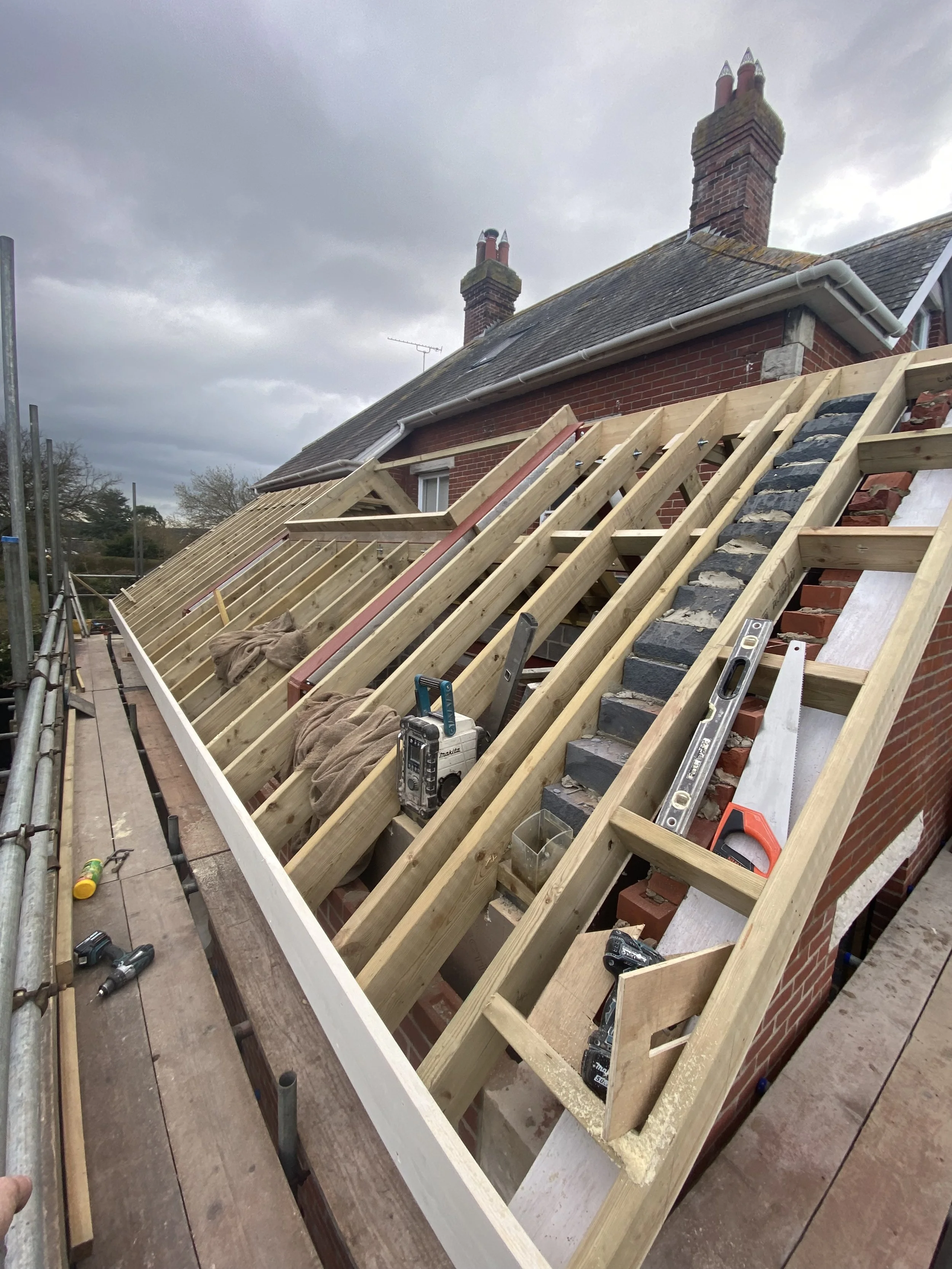 Building a roof frame on a house with tools and construction materials visible on the site.