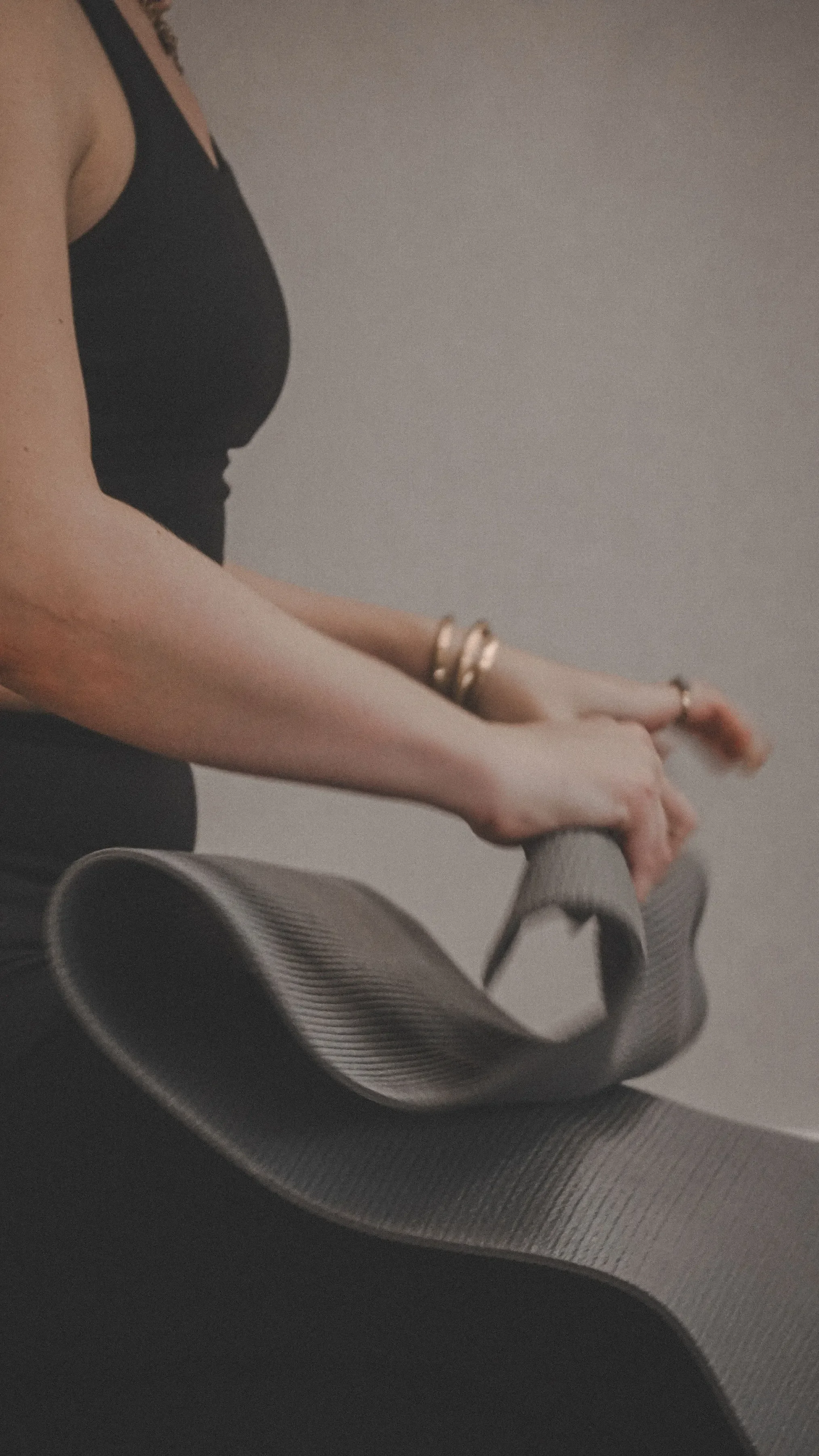The image shows a person in a black tank top sitting on a yoga mat, with their hands resting on a rolled-up yoga strap.