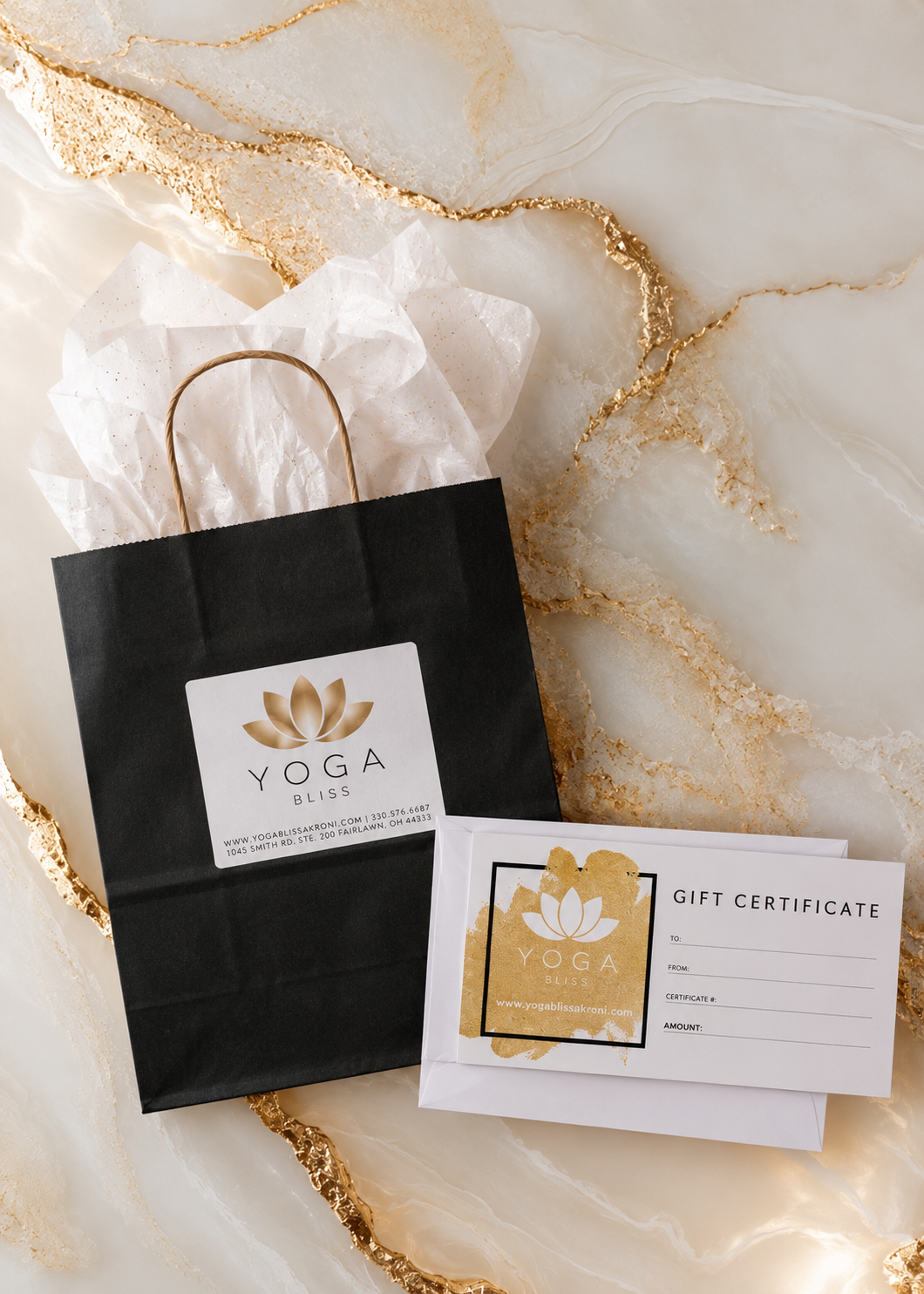 A black gift bag with a gold and white yoga bliss logo, tissue paper, and a gift certificate for Yoga Bliss on a marble surface with gold veins.
