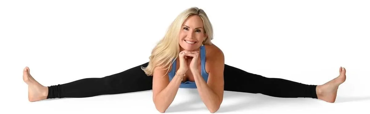 A woman performing a split exercise on the floor with a smile, wearing a blue tank top and black leggings.