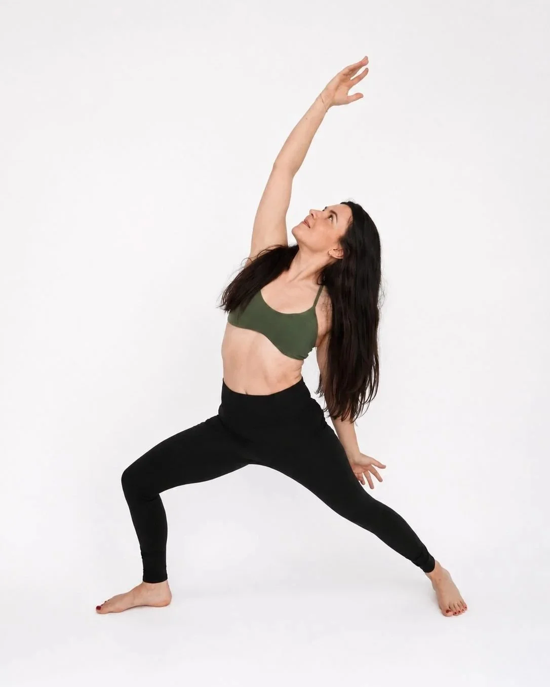 A woman practicing yoga in a wide stance, reaching upward with one arm, against a plain white background.
