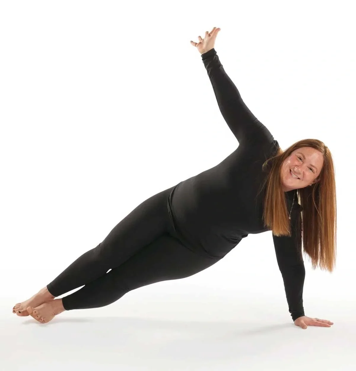 A woman performing a side plank yoga pose on a white background, with one arm extended upward and a smile on her face.