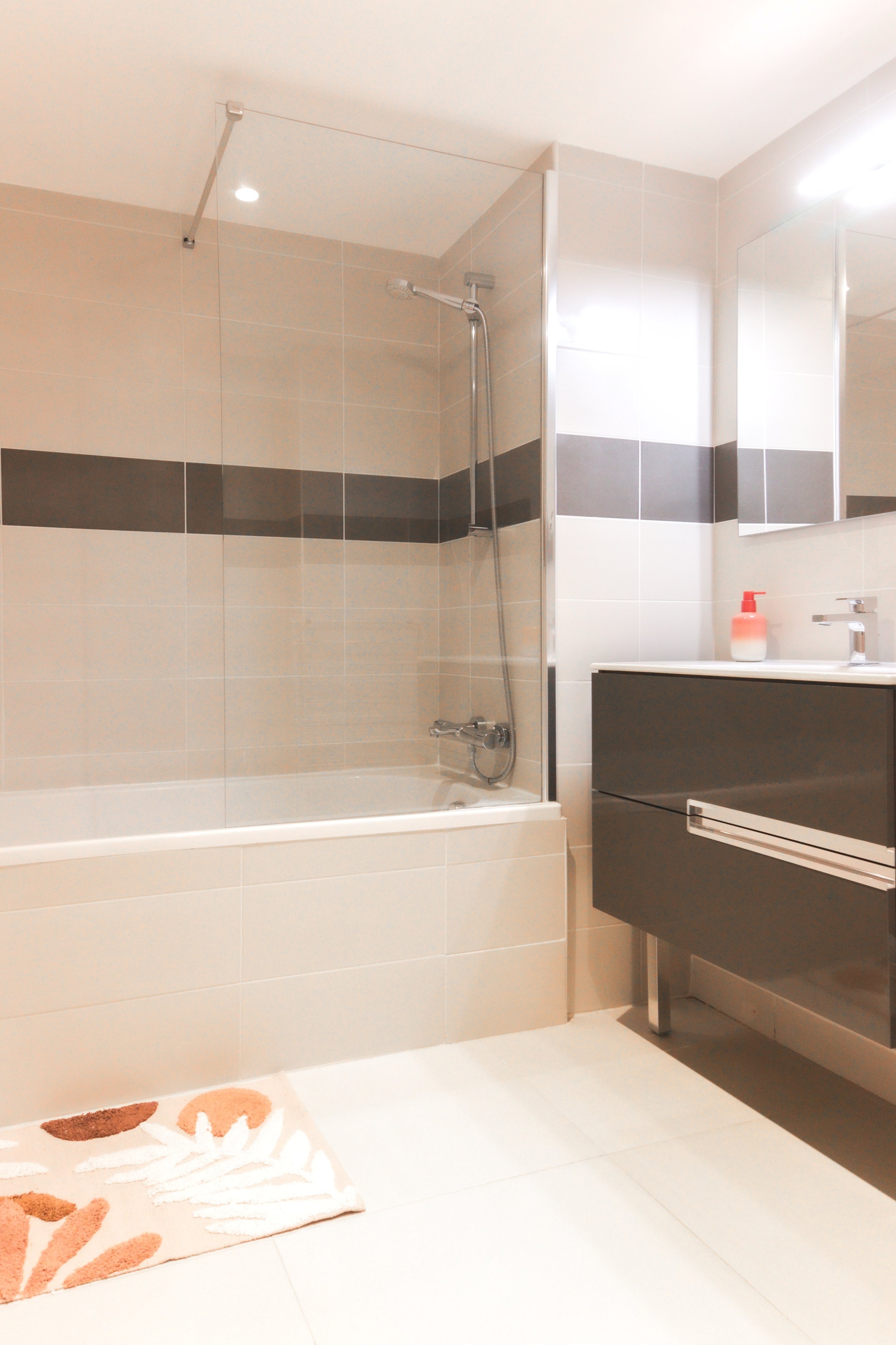 Modern bathroom with shower tub, gray vanity, soap dispenser, and a decorative rug.