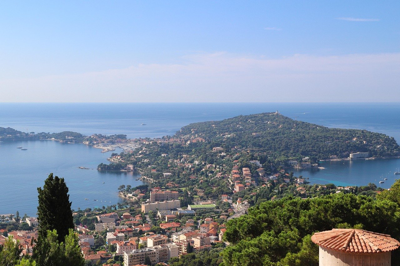 A scenic view of a coastal town on a peninsula with green hills, water, and boats, overlooking the ocean on a clear day.