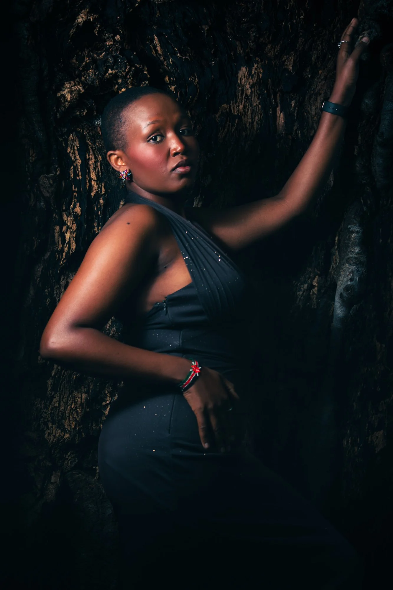 A woman in a dark, elegant dress poses against a textured, dark background, looking confidently at the camera.