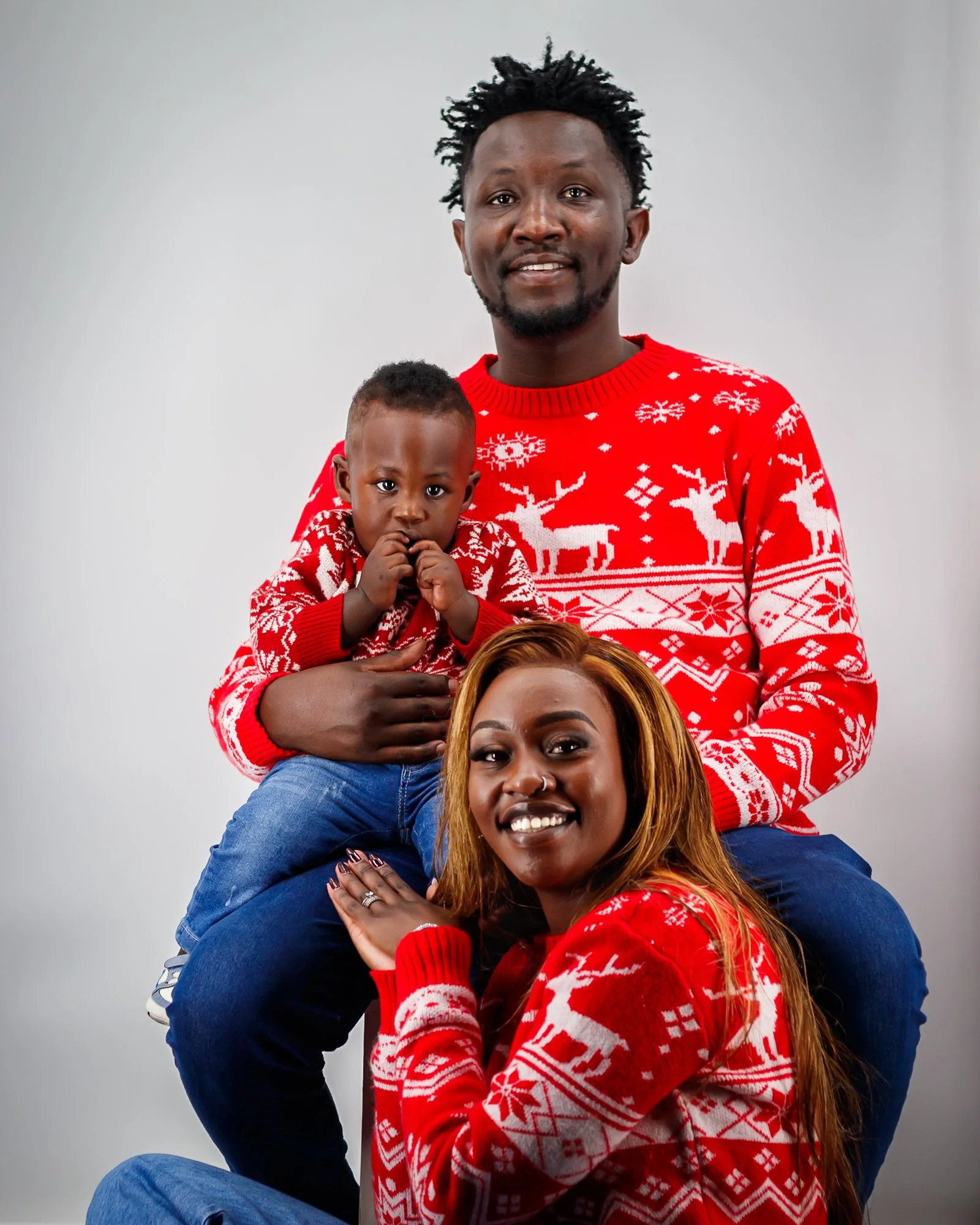 Family of three in Christmas sweaters, smiling, against a plain light gray background.