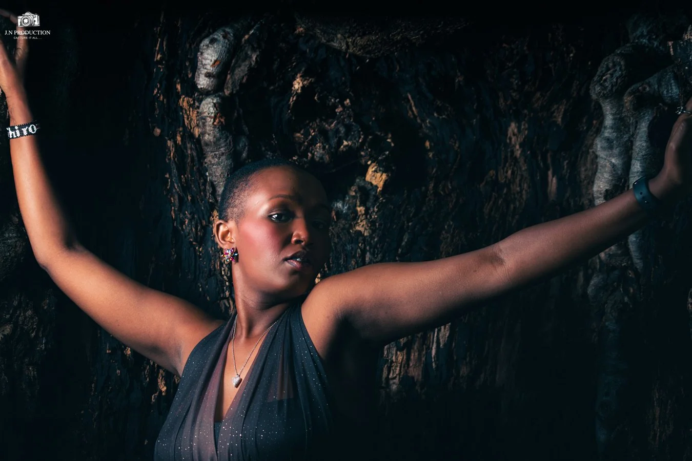 A woman with short hair and dark skin posing with arms outstretched against a dark, textured background.