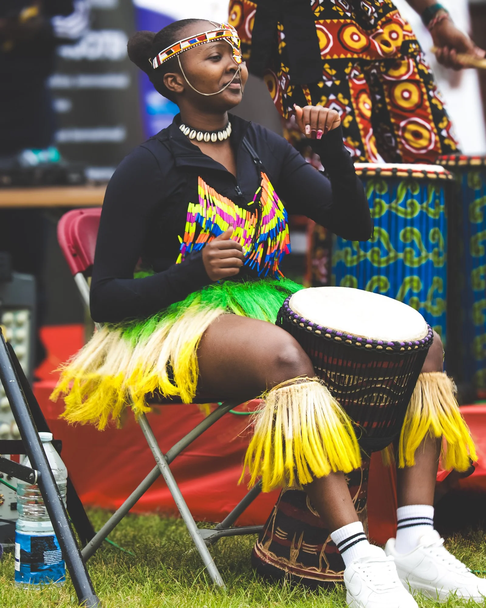 Young woman dressed in traditional African attire playing a drum at a cultural event.