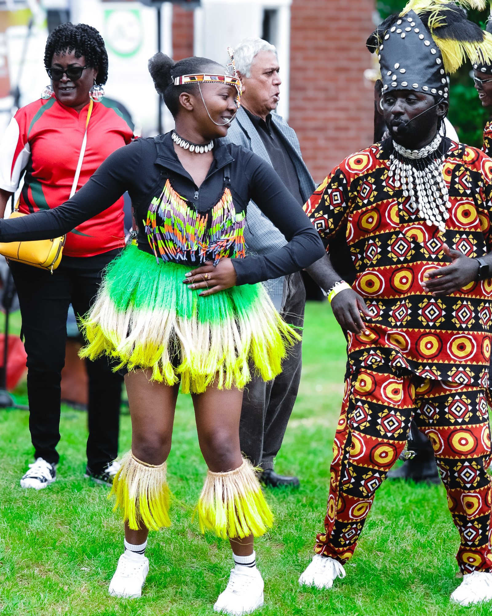 People dressed in traditional African attire, dancing outdoors on grass.