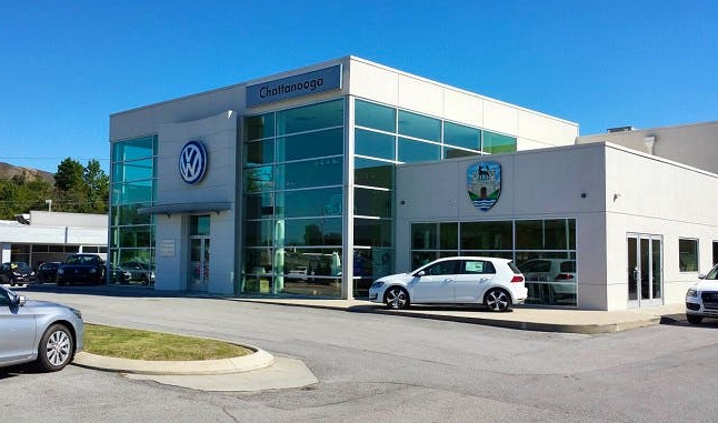 Volkswagen car dealership with large glass windows, Volkswagen logo, and a Chattanooga sign on the building, with a white car parked outside.