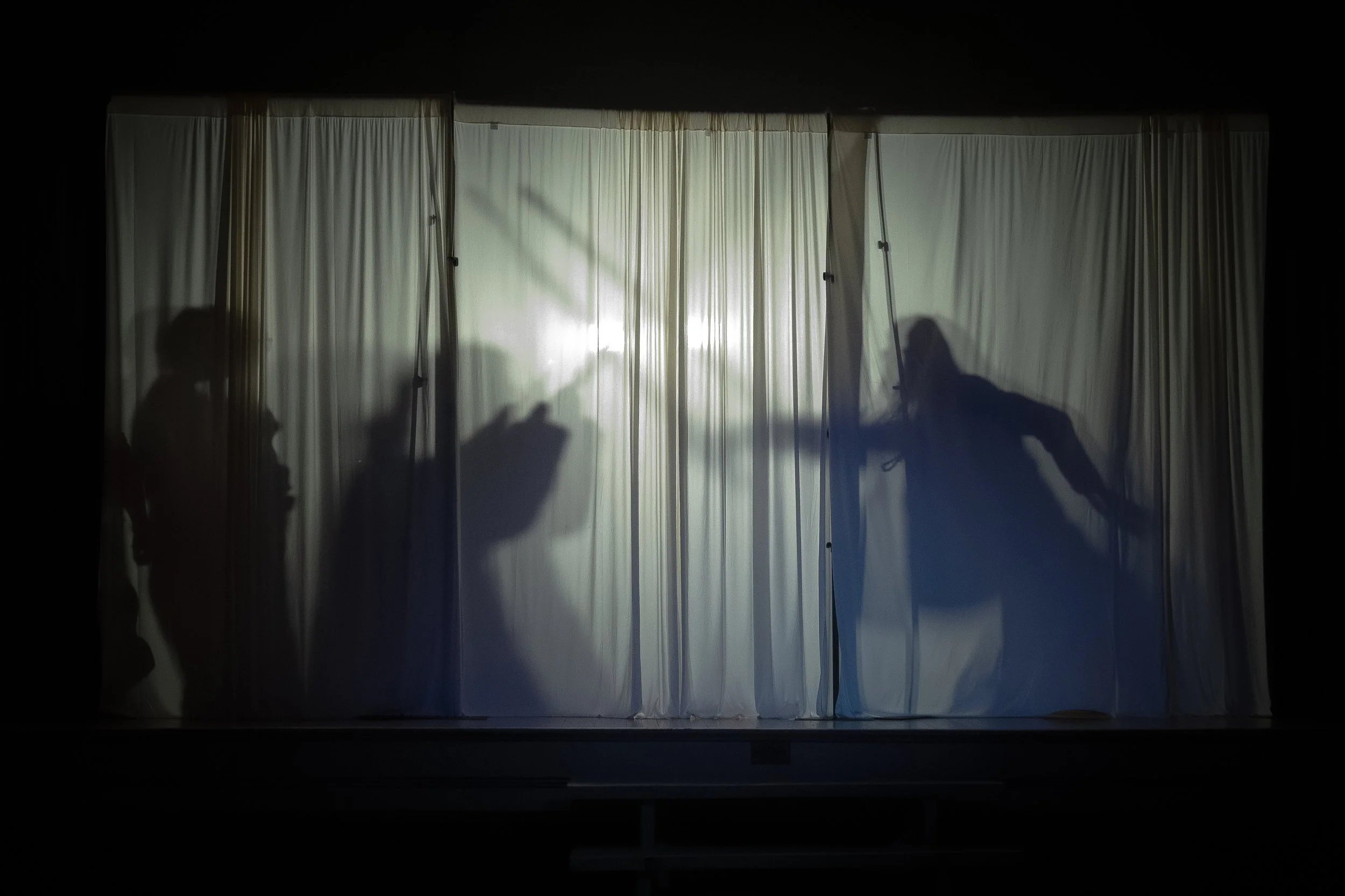 Shadows of four people behind a white curtain on a stage.