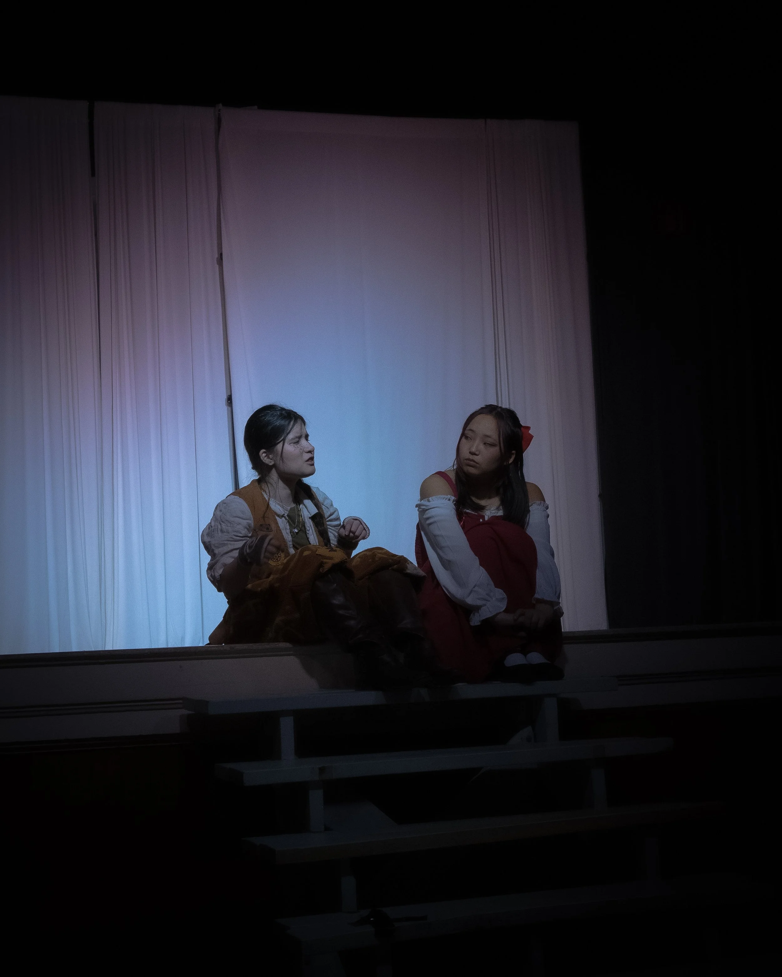 Two women sitting on a stage in front of a white curtain, engaged in conversation.