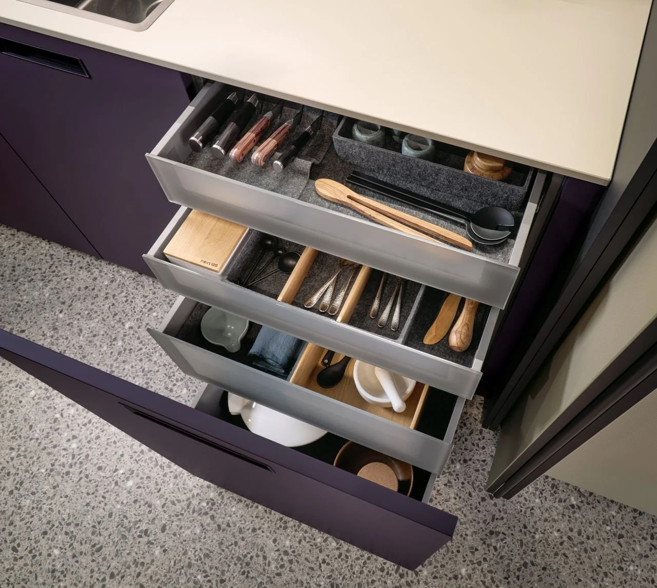 Open kitchen drawer with utensils, knives, spoons, and small accessories organised inside.