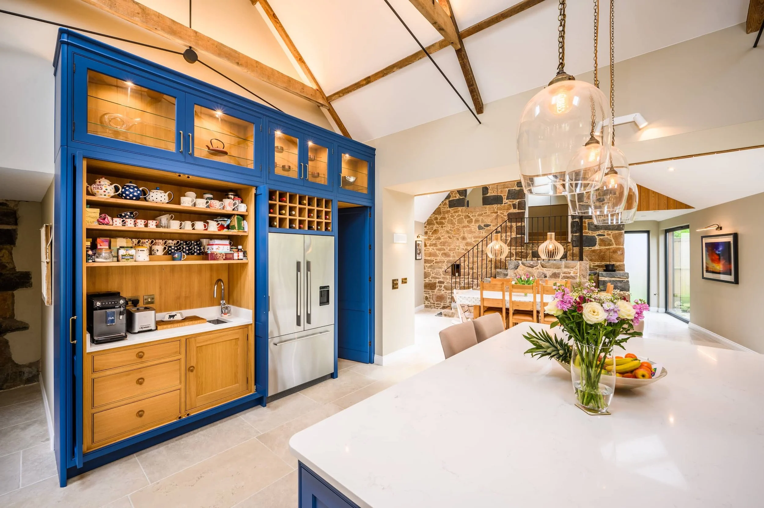 Shaker kitchen with blue cabinets, a white countertop with a flower vase, and a stone staircase in the background.