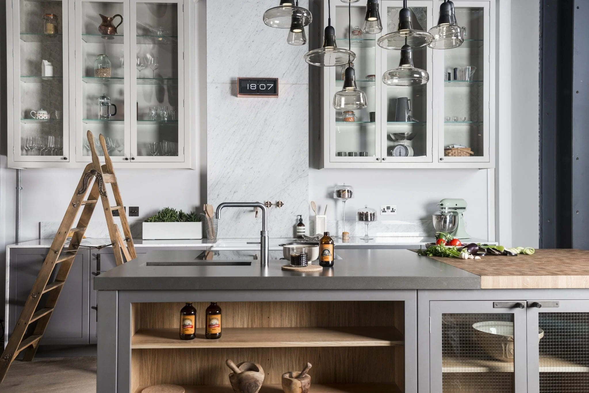 Modern kitchen with white cabinets, glass-front doors, pendant lighting, kitchen island with a sink, vegetables, and kitchen essentials.