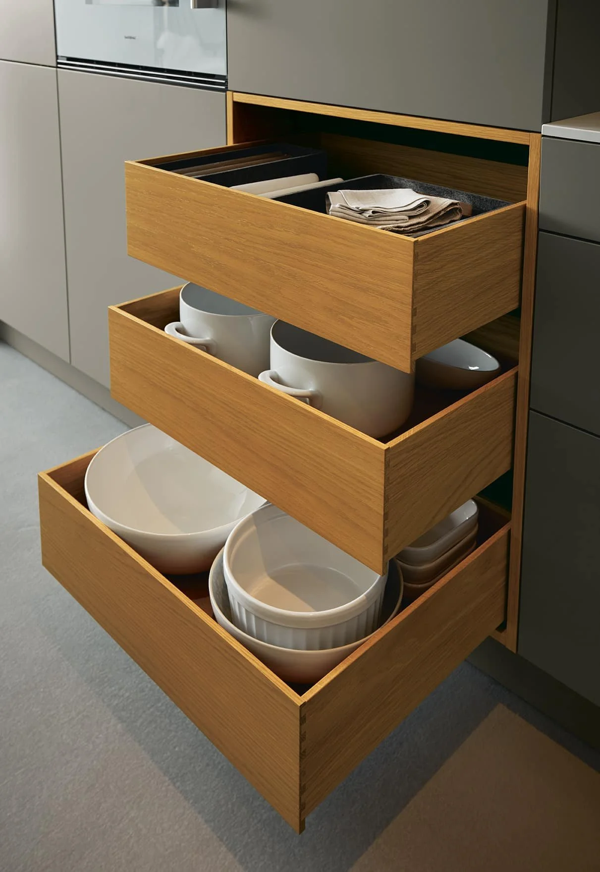 Open kitchen drawer filled with neatly stacked bowls, cups, and kitchen linens.