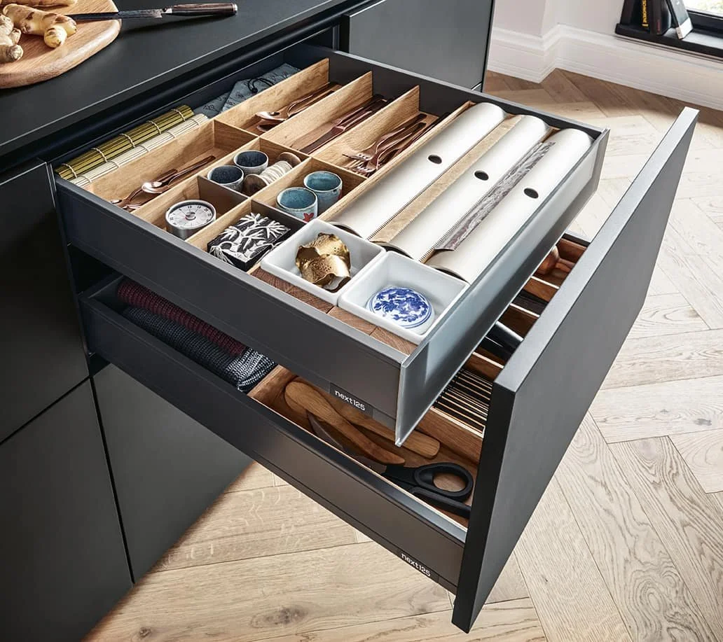 Open kitchen drawer containing utensils, napkins, small bowls, and various kitchen tools organised in compartments.