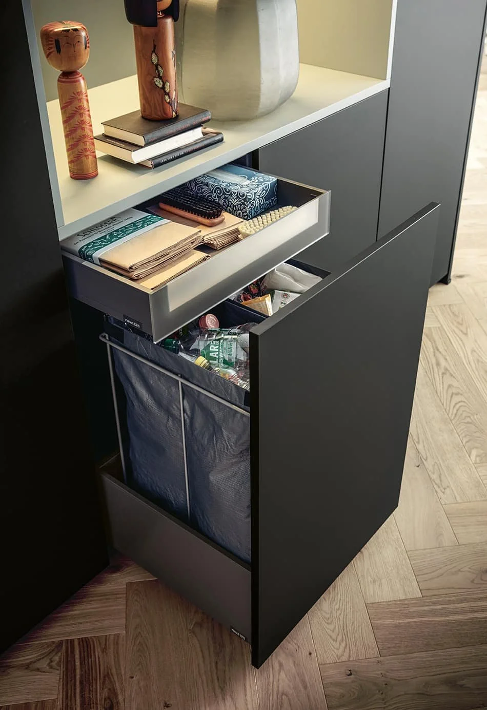 A black and white cabinet with an open drawer containing paper tissues and a drawer below storing bottled water and snacks.