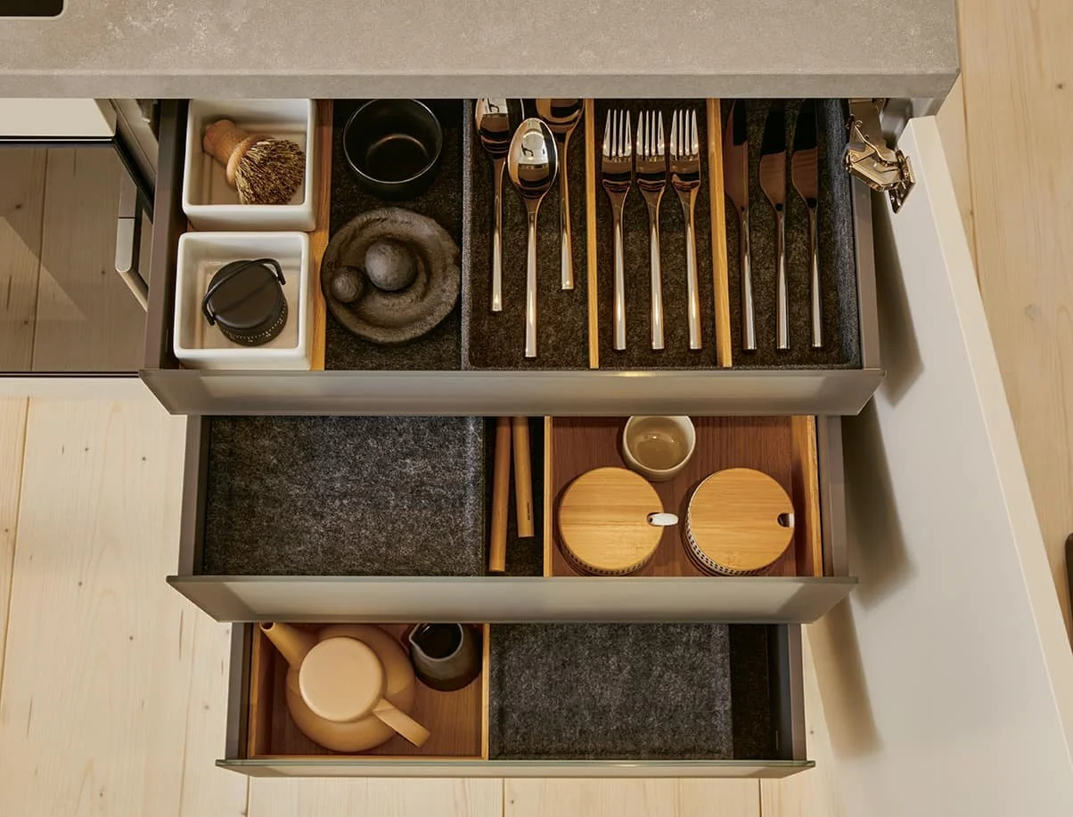 Open kitchen drawer with organised utensils, bowls, a teapot, and a small bowl.