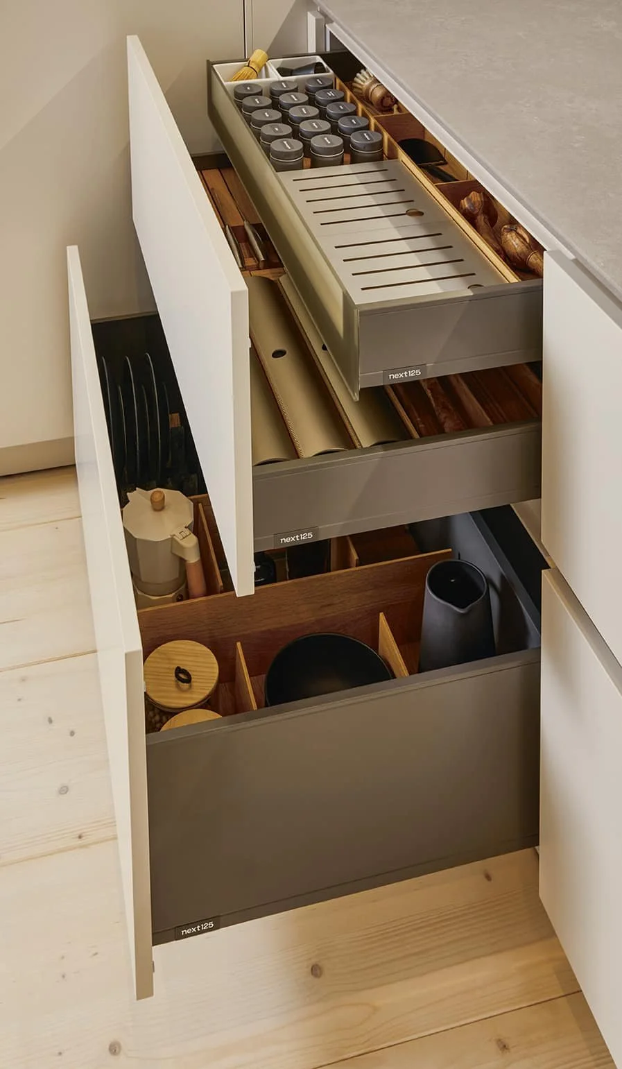 Open kitchen drawers featuring kitchen storage and organised items, including spice jars, utensils, cutting boards, bowls, and containers.