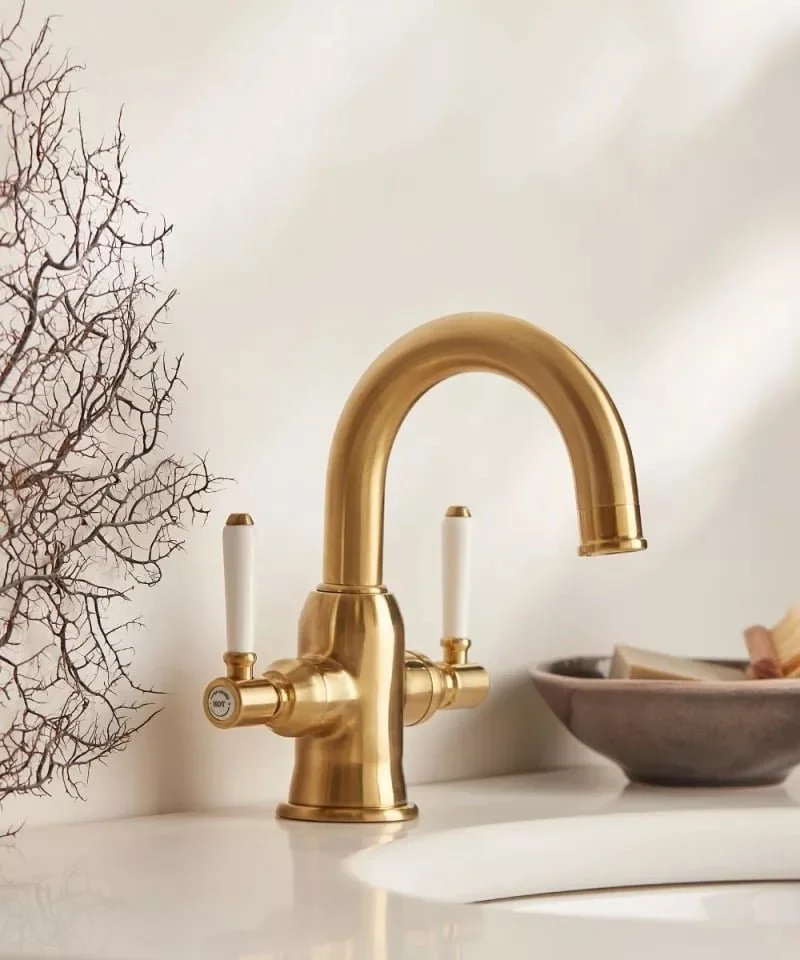 Close-up of a gold kitchen faucet with white handles on a white countertop.