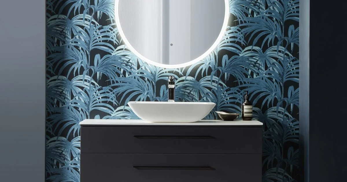 Modern bathroom vanity with a round mirror, a vessel sink, a soap dispenser, and a decorative bowl, set against a blue tropical leaf-patterned wallpaper.