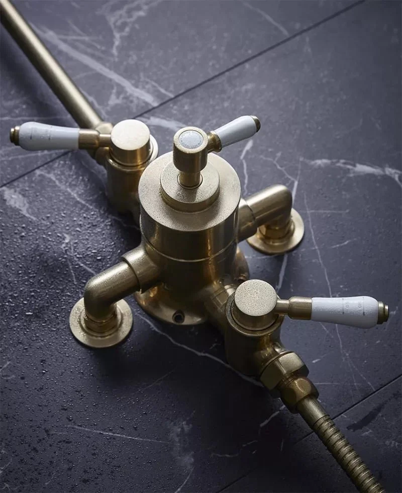 A vintage brass kitchen faucet with multiple handles and a hose attachment, placed on a dark marble or tiled surface.