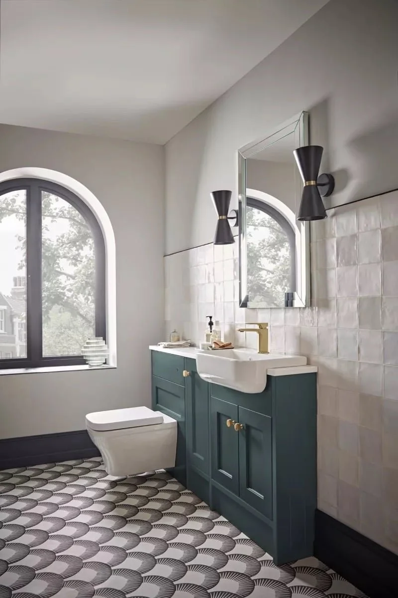 Shaker bathroom with a teal vanity, white sink, gold faucet, black wall sconces, arched window, and patterned black and white floor tiles.