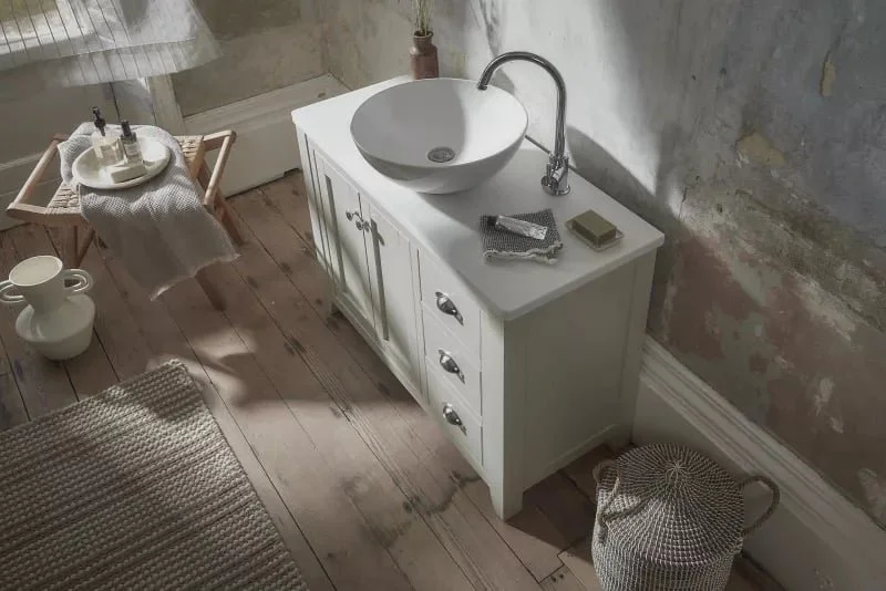 A small traditional bathroom vanity with a white sink and a faucet, a mirror, and a few toiletries on top.