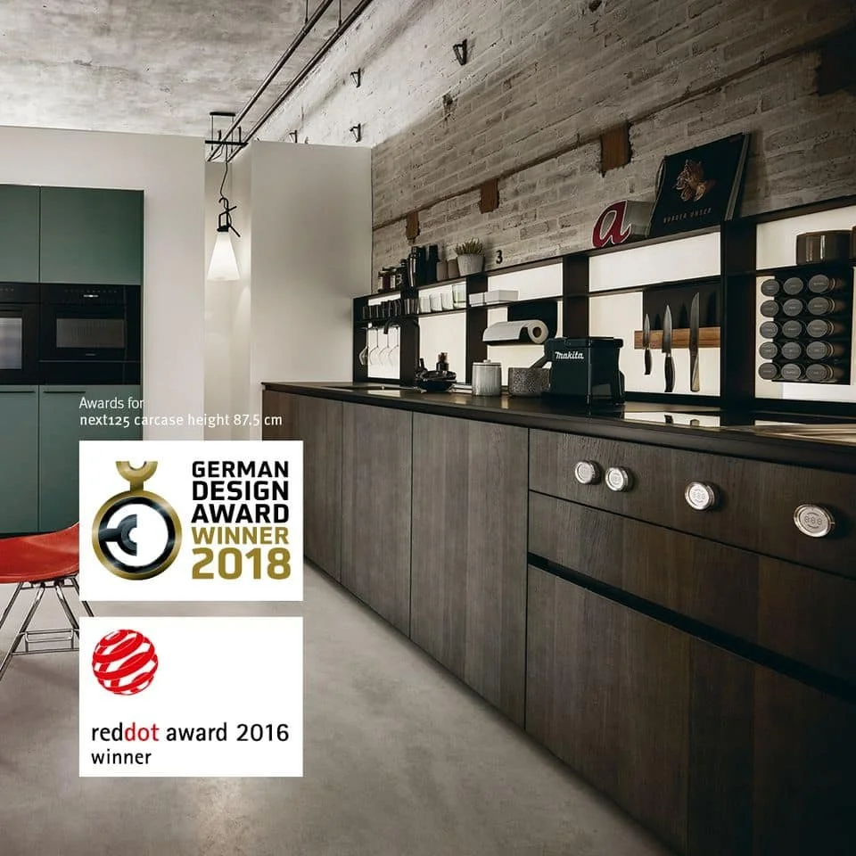 Modern kitchen with wooden cabinets, black shelving, and culinary tools, awarded the German Design Award in 2018 and Red Dot Award in 2016.