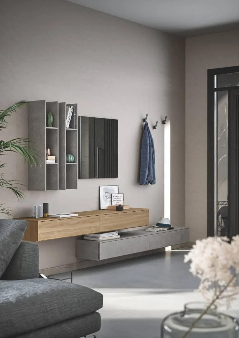 Modern living room with beige walls, a grey sofa, wall-mounted shelving with decorative items, a wall mirror, coat hooks with a blue towel, and a sliding glass door.
