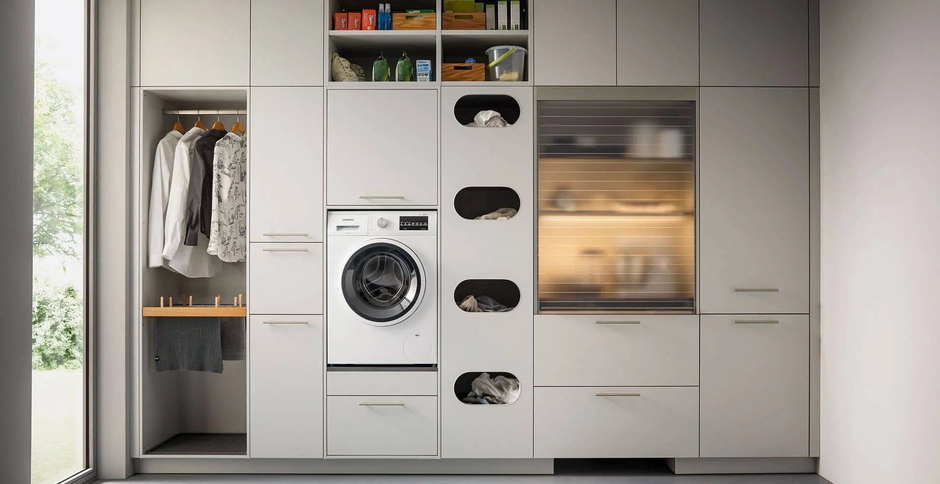 Modern utility room with built-in cabinets, open wardrobe section with hanging clothes, washing machine, and various storage spaces.