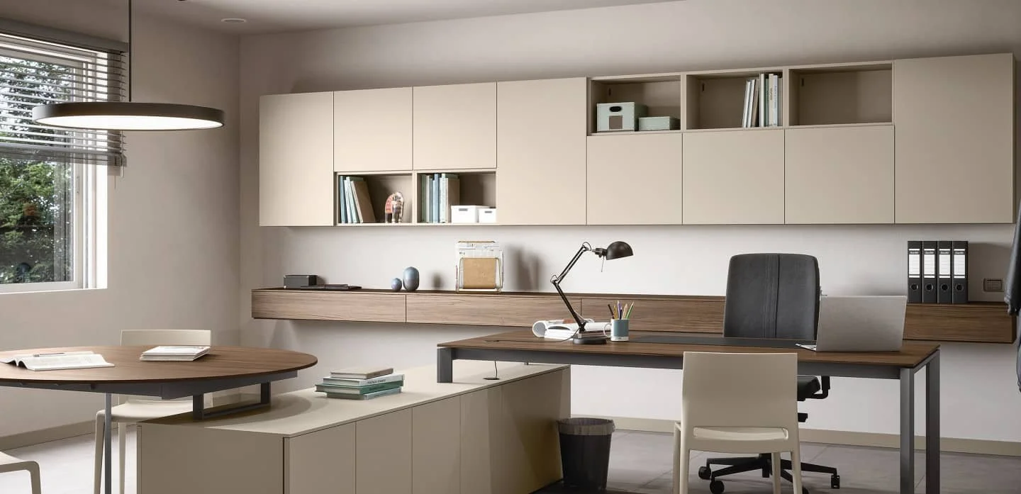 Modern home office with a wooden desk, an ergonomic office chair, shelves with books and storage boxes, a window with blinds, and a grey side table with books.